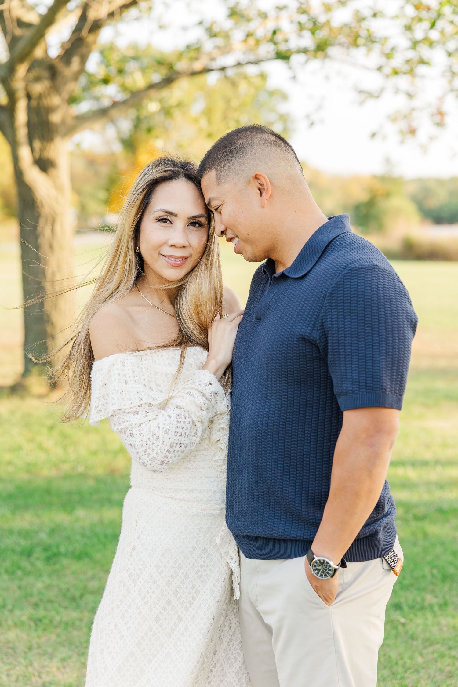 A couple in white and navy blue outfits share intimate moments during a romantic outdoor photo session at sunset. Busse Woods