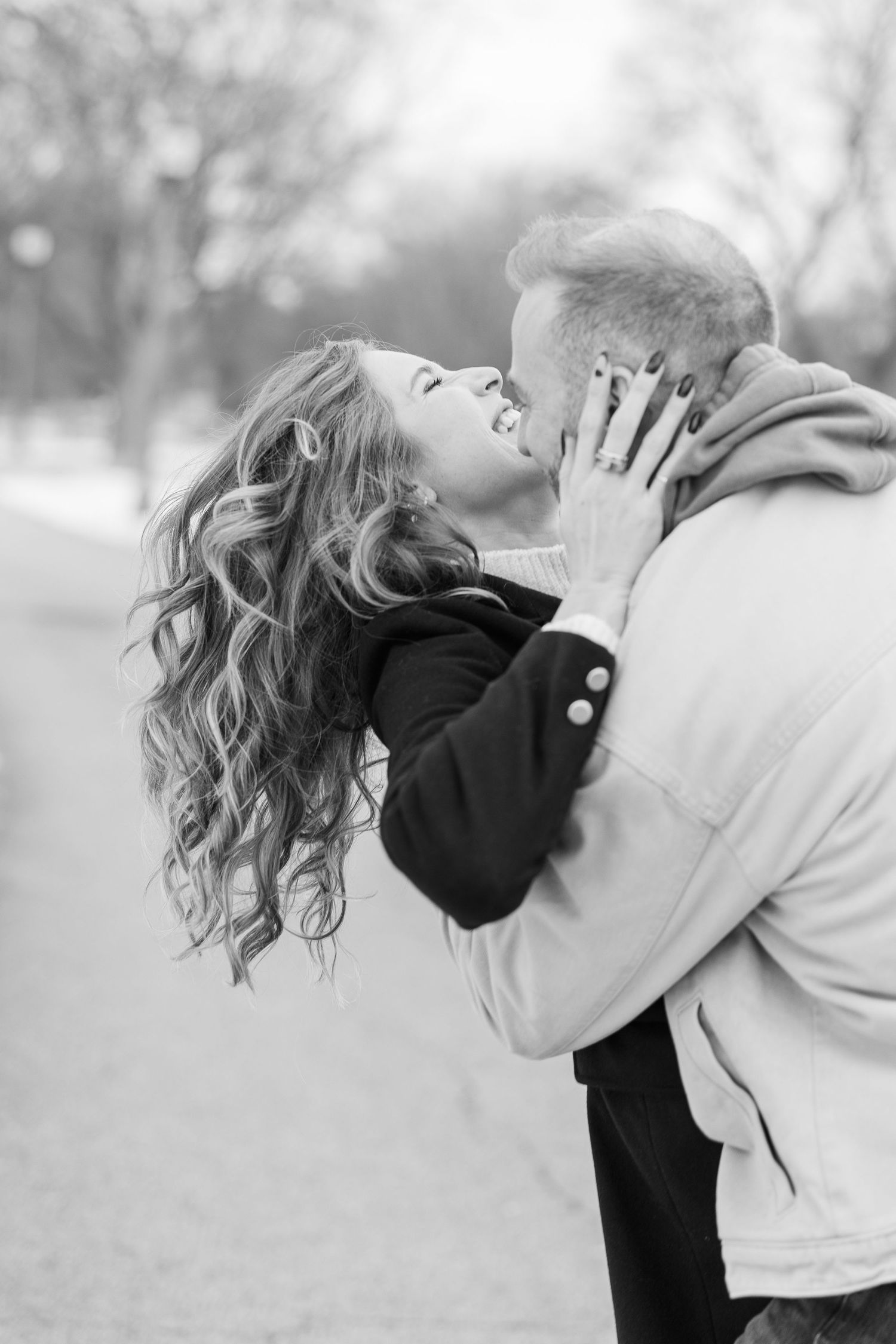 A romantic black and white photo shows a couple embracing outdoors, with her curly hair flowing as she leans back joyfully.