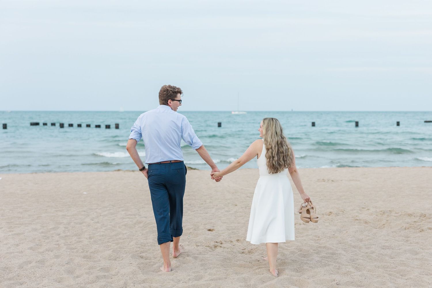 Elizabeth and Joe walking hand-in-hand along North Avenue Beach, with gentle waves and a soft sunset in the background