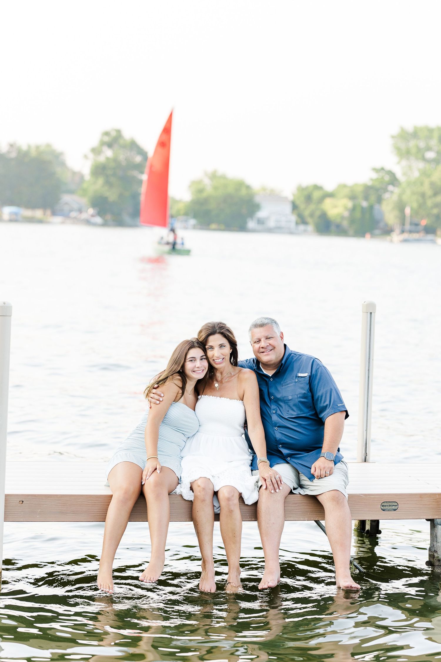 Family sitting on dock with sailboat during Pistakee Lake family photos in Johnsburg, Illinois