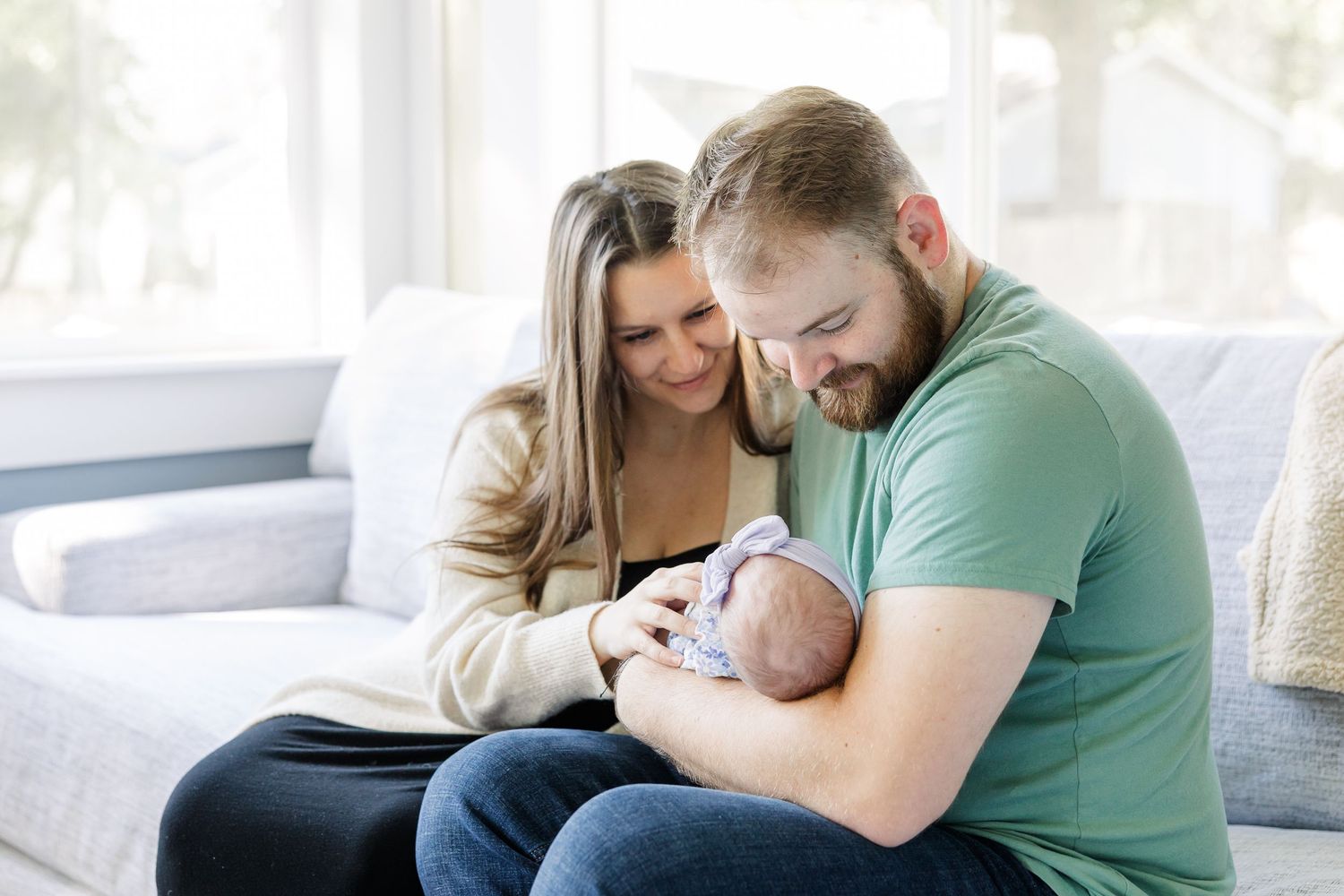 Happy couple sitting on a couch together lovingly cradling their newborn baby.