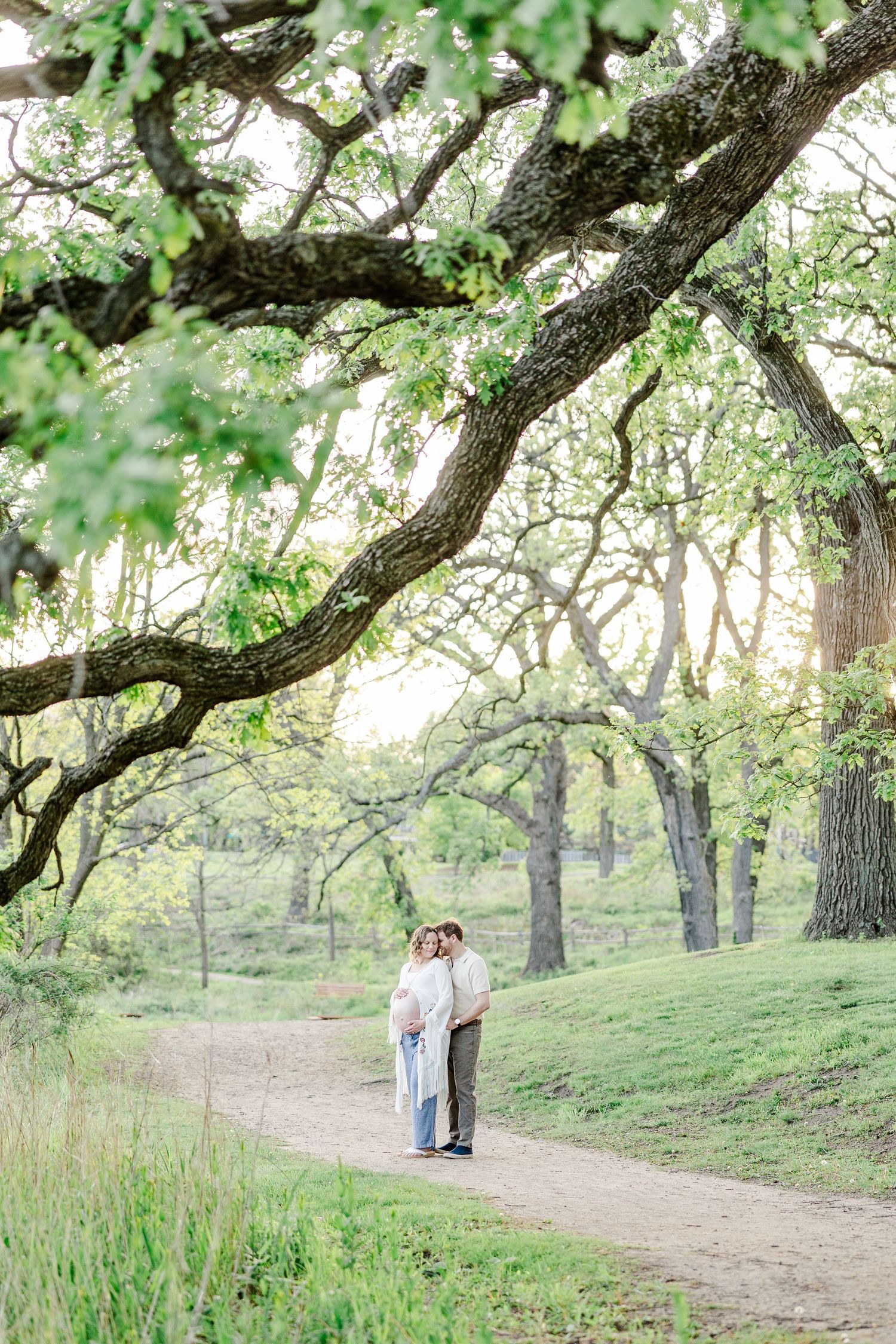 Expecting parents walking under spring trees during a maternity session at Veterans Acres Nature Preserve.