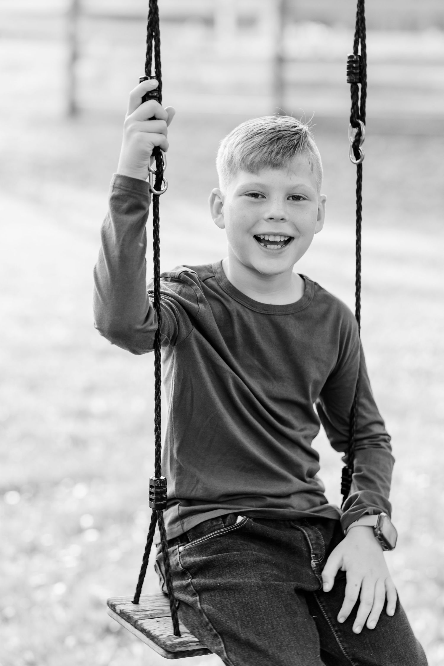 Black and white portrait of a smiling boy on a tree swing.