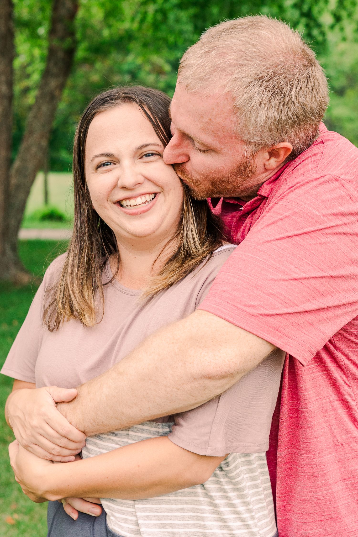 A joyful embrace captured between a couple outdoors with green foliage in the background.