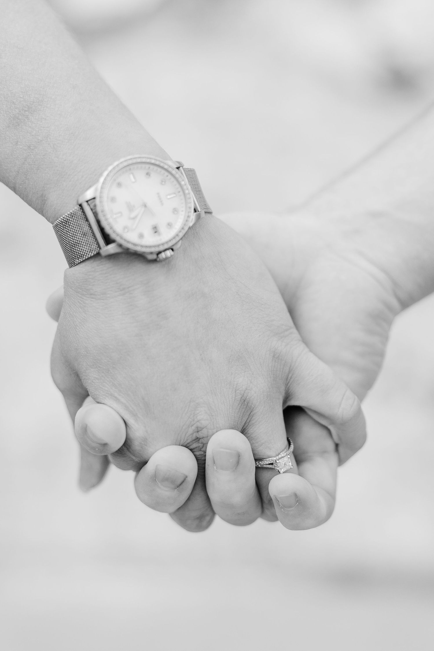 Two hands clasped together, with one wearing a silver watch and the other a delicate ring.