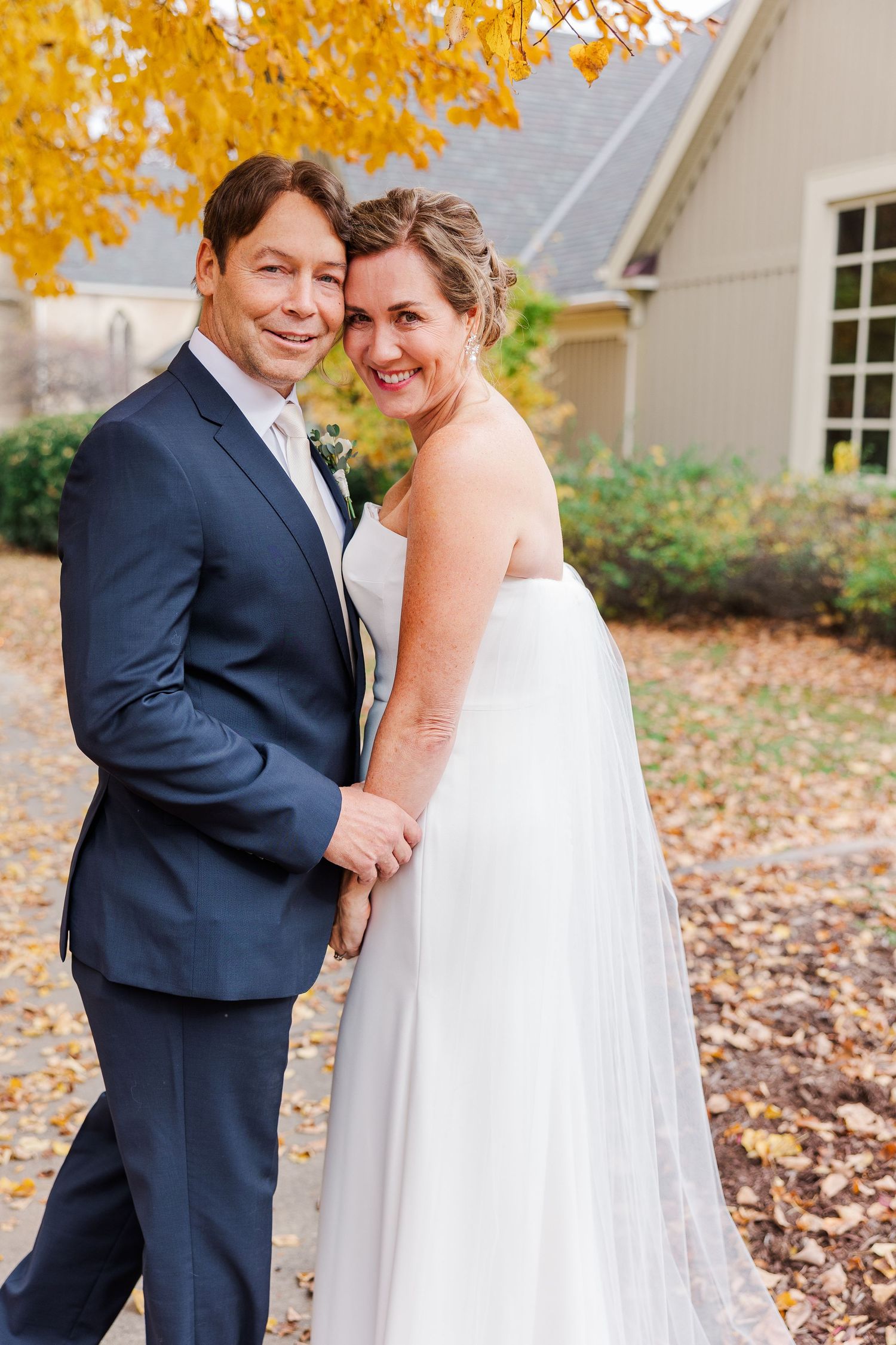 Candid wedding portrait of couple embracing under golden fall leaves.