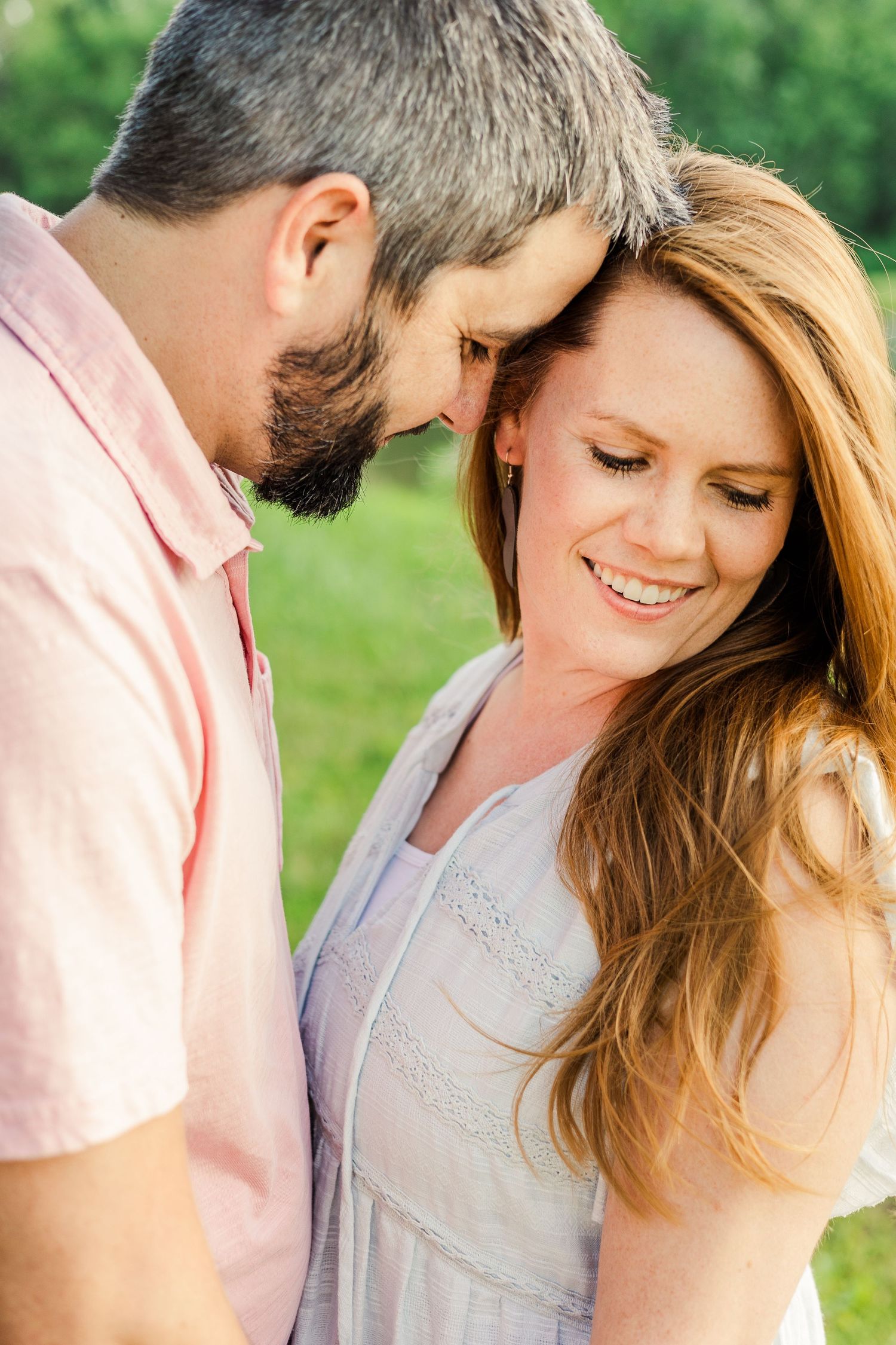 A couple in soft pink and white clothes share a close romantic moment in a garden setting.