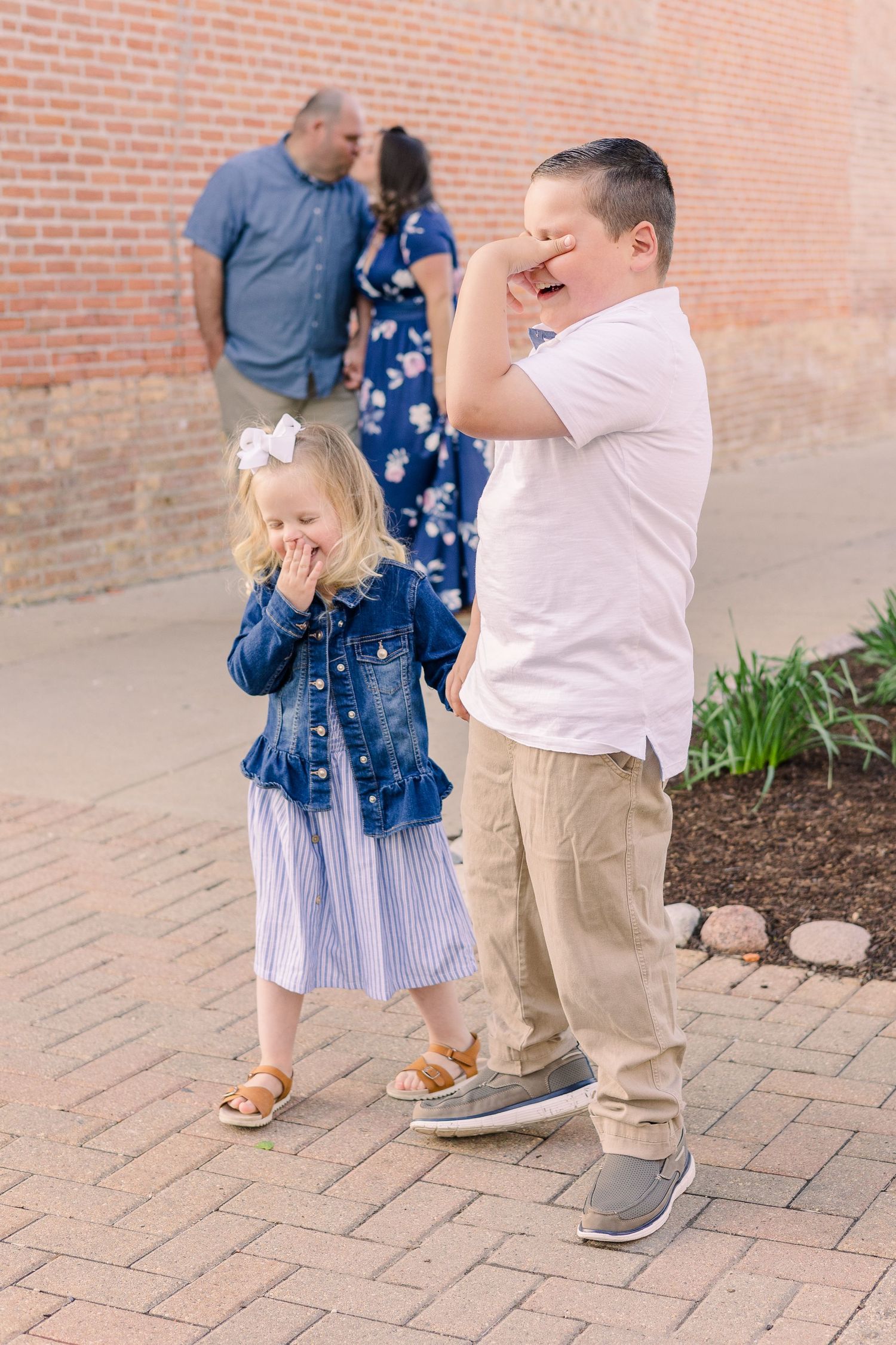 Playful family members covering faces and laughing on brick pathway.