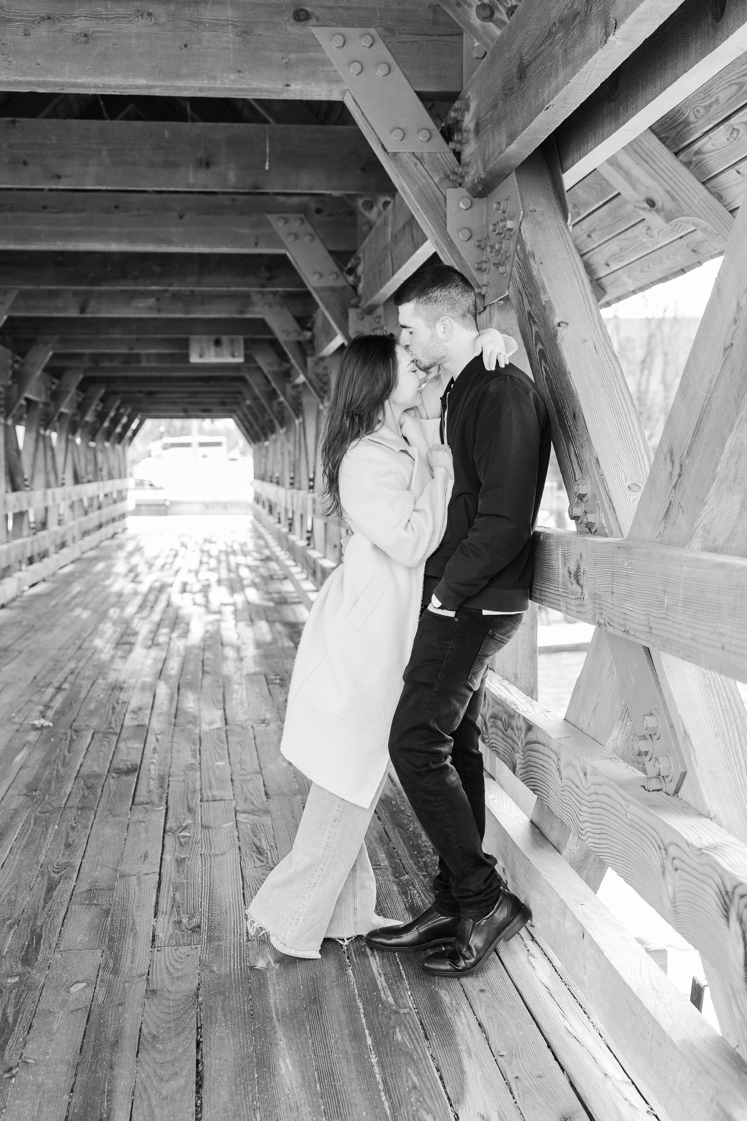 A black and white photo of a couple kissing in a covered wooden bridge.