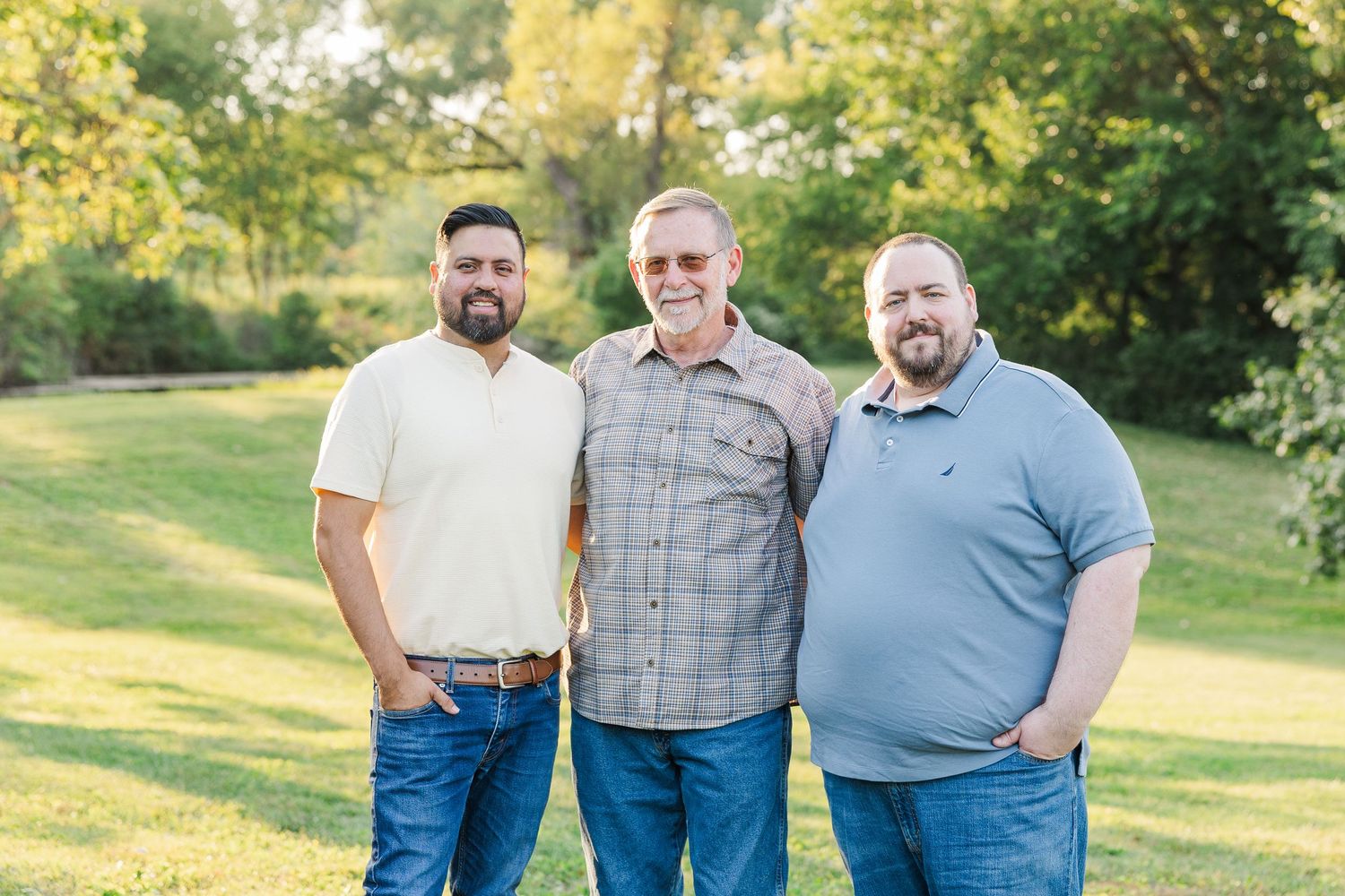 A family poses together outdoors in a park wearing coordinated blue and gray outfits during a sunny autumn day. Sorg family portraits