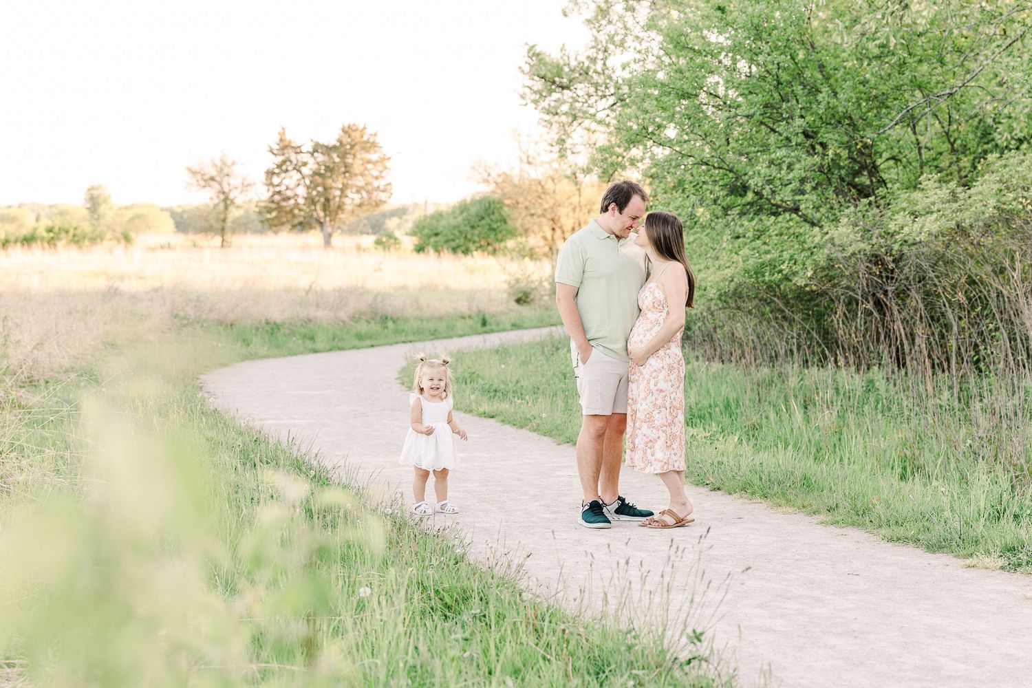 A loving family walks together on a winding path through a scenic natural landscape at sunset.
