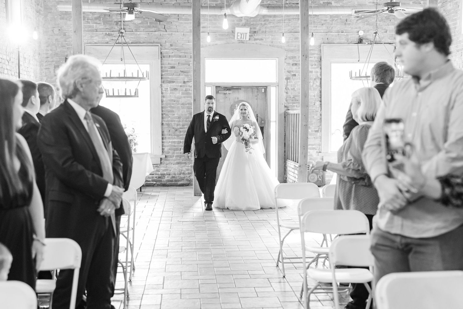 Black and white photo of wedding ceremony processional in industrial brick venue.