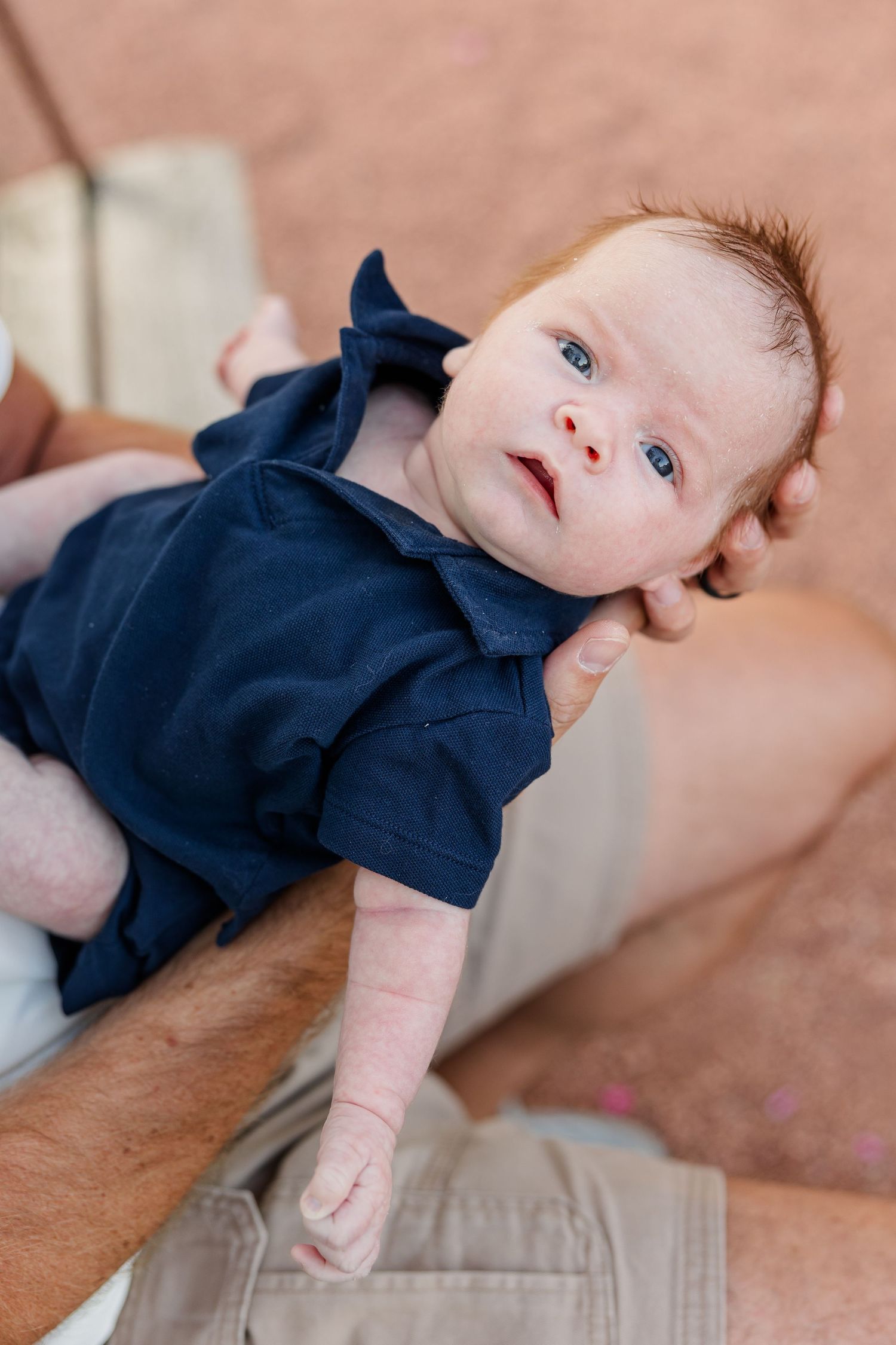 Newborn Lincoln looking toward the camera while resting comfortably in Andrew’s arms.