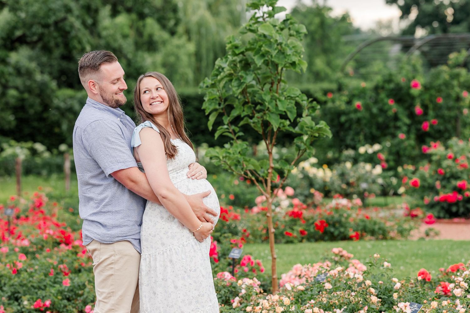Expecting parents laughing together in the rose garden during their maternity session