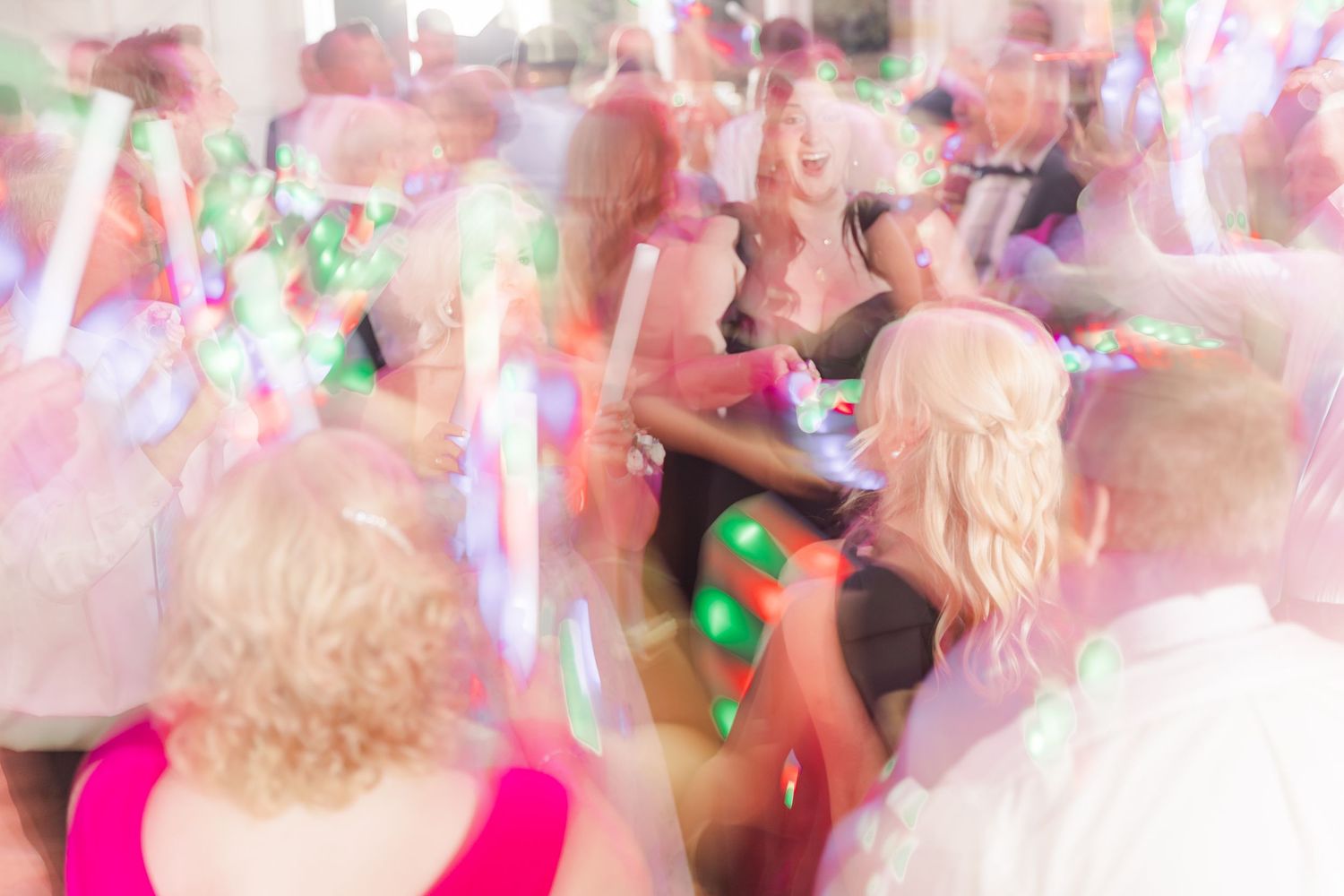 Wedding guests dance under colorful glowing lights creating a festive blurred motion effect on the dance floor.