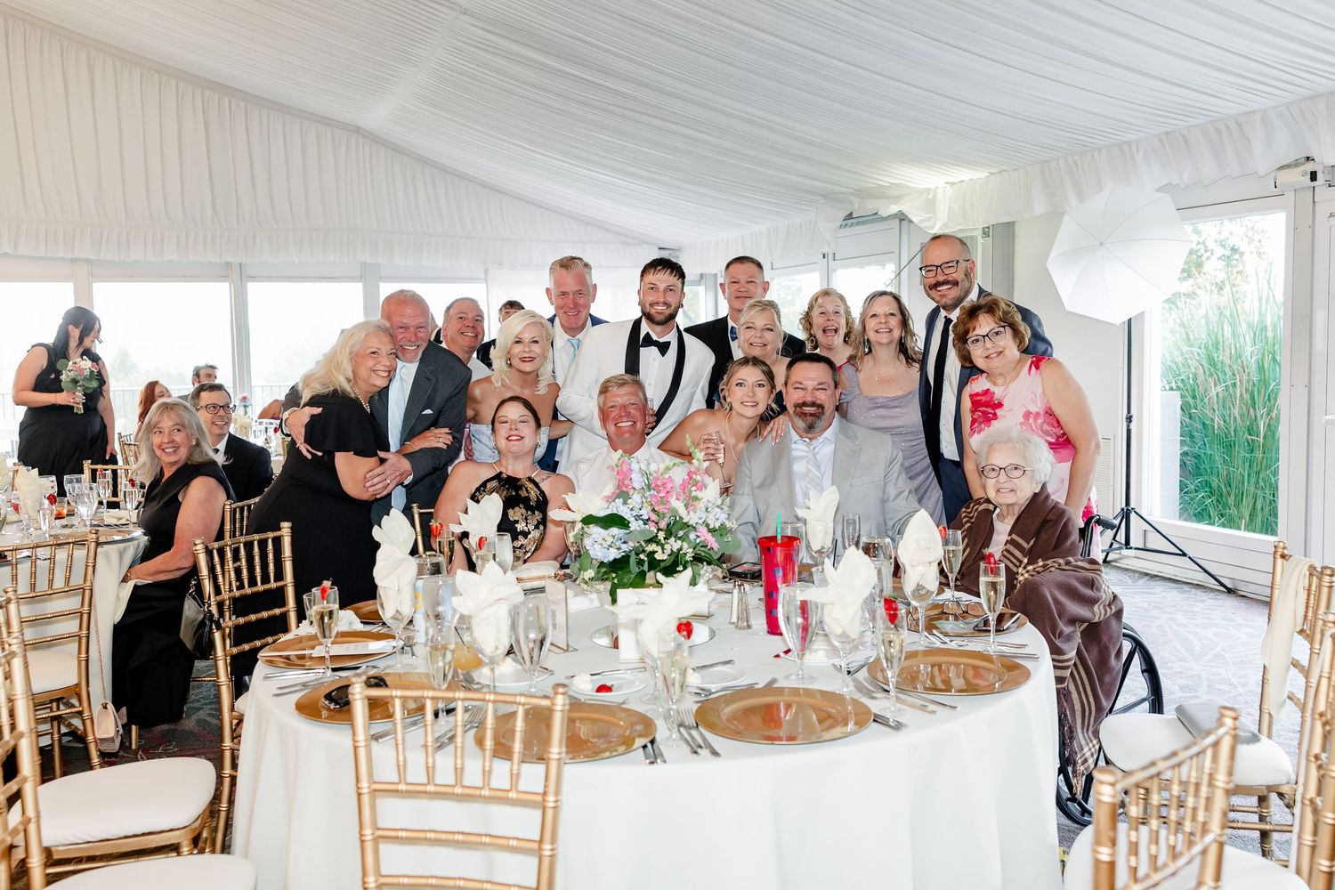 Large group of wedding guests posing together at a reception venue with gold-themed table settings.