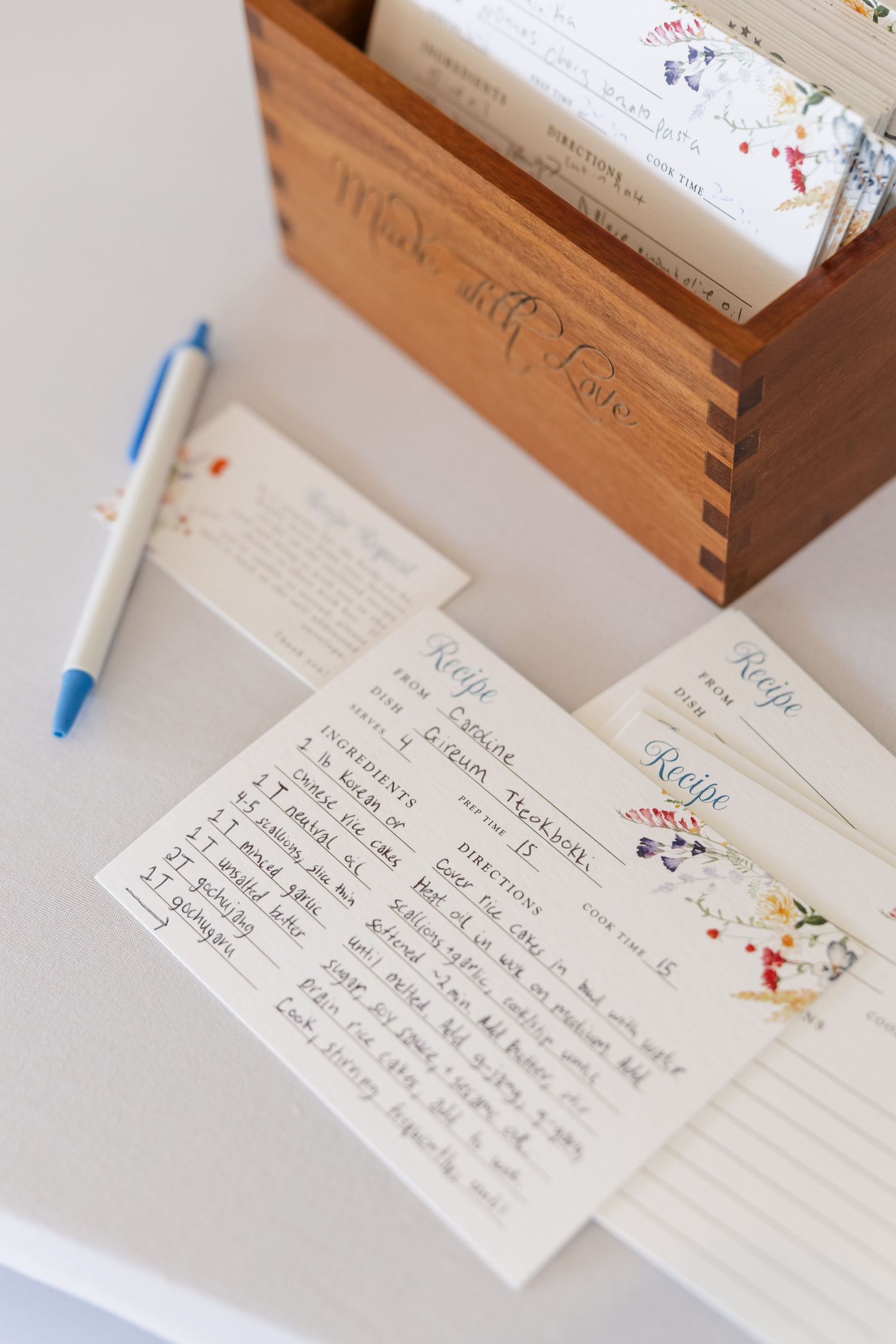 Handwritten recipe cards beside a wooden Made with Love recipe box at a bridal shower.