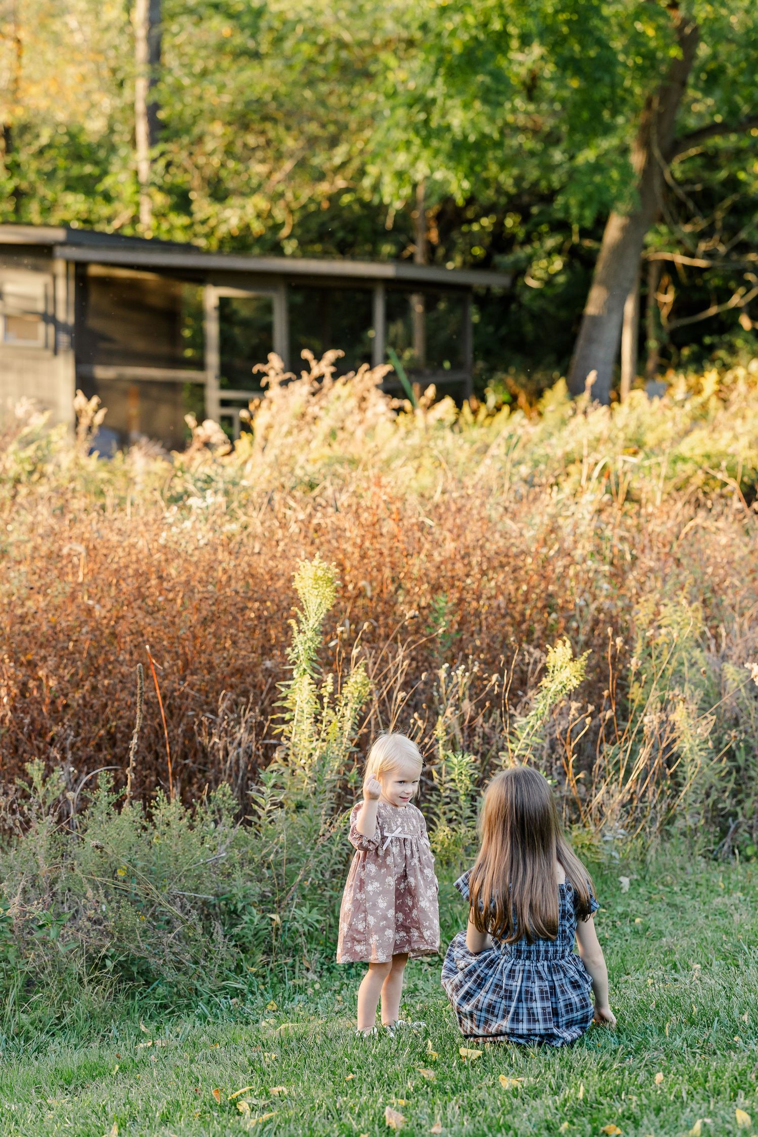 Two sisters beside tall grasses near their backyard chicken coop in St. Charles, IL.