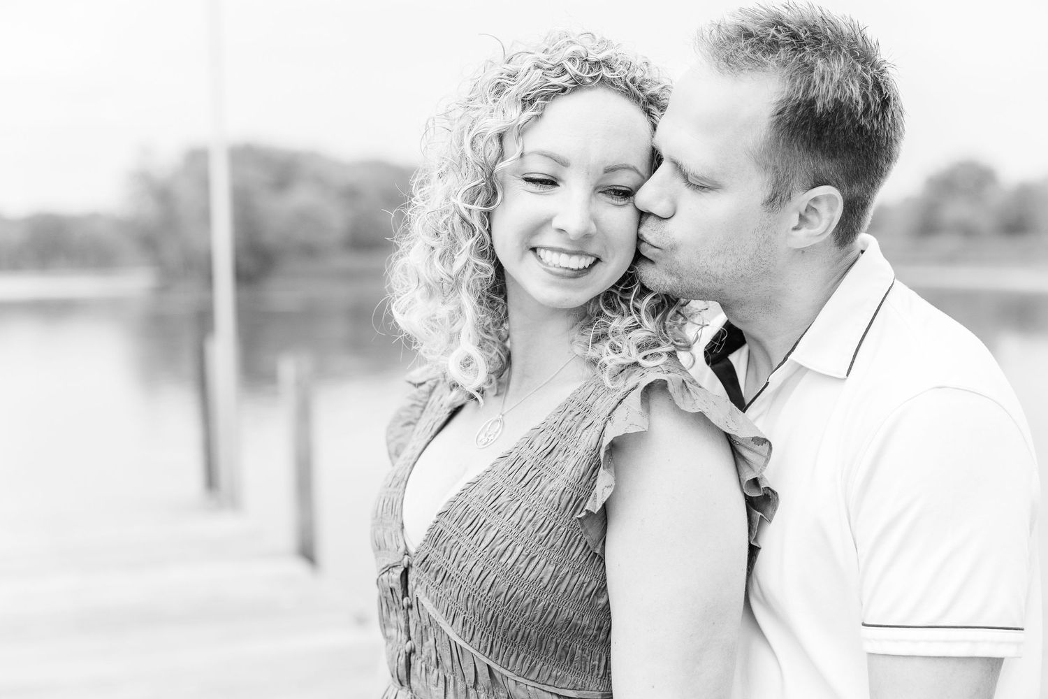 A black and white portrait captures an intimate moment on a lakeside dock.