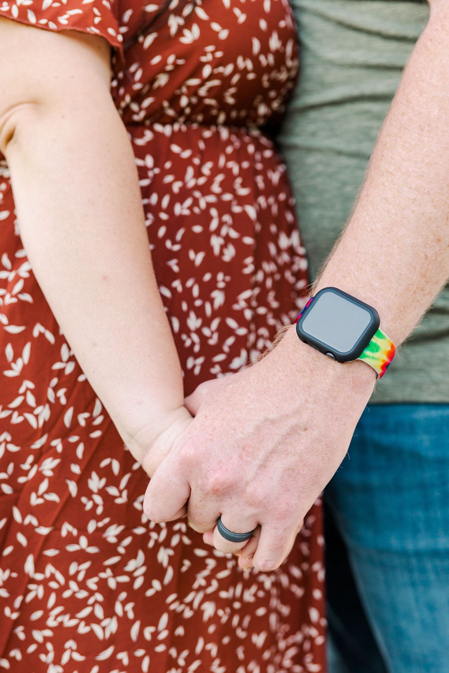 A close-up of holding hands with one person wearing an Apple Watch with rainbow band.