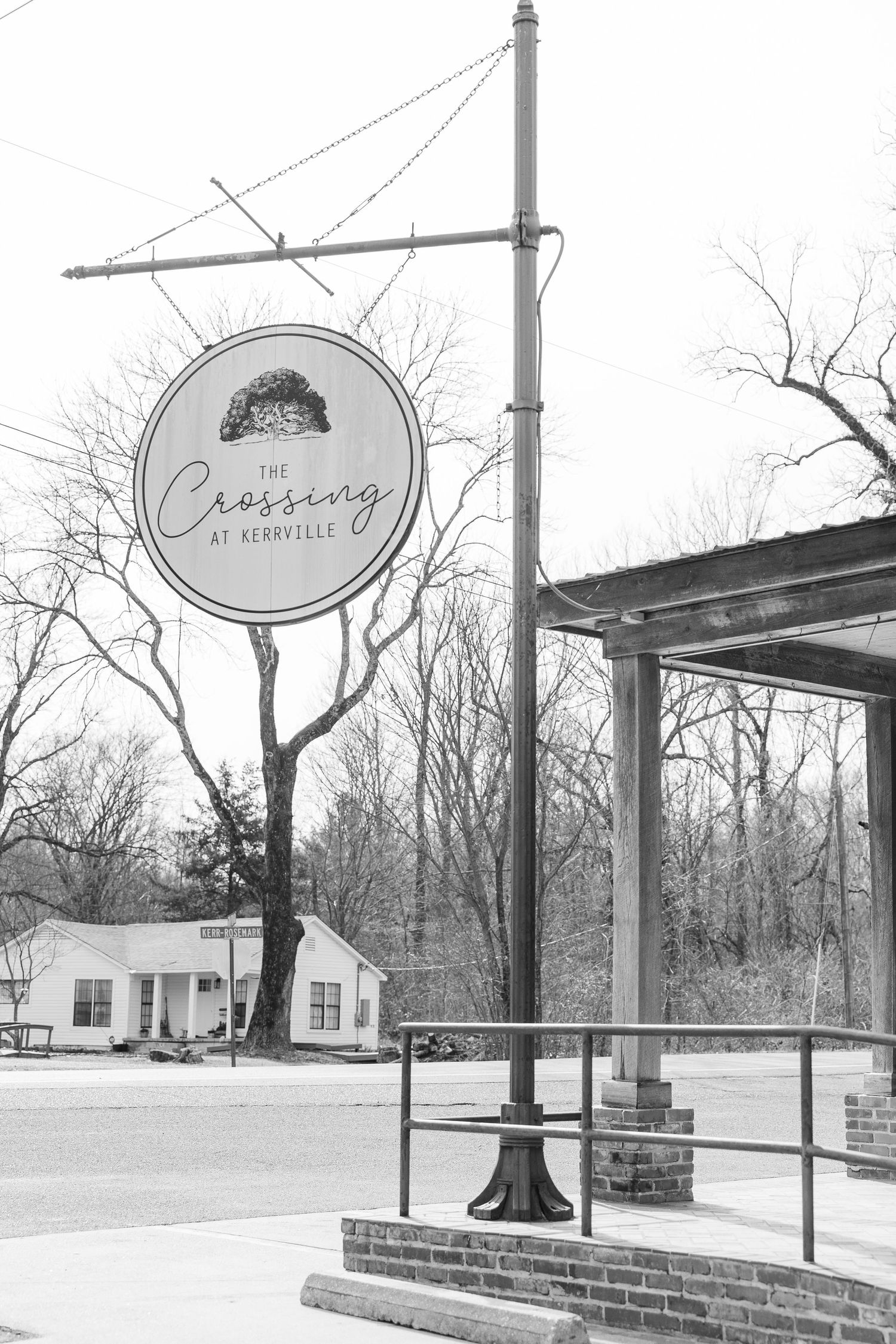 A black and white photo of The Crossing restaurant sign mounted on a vintage pole.