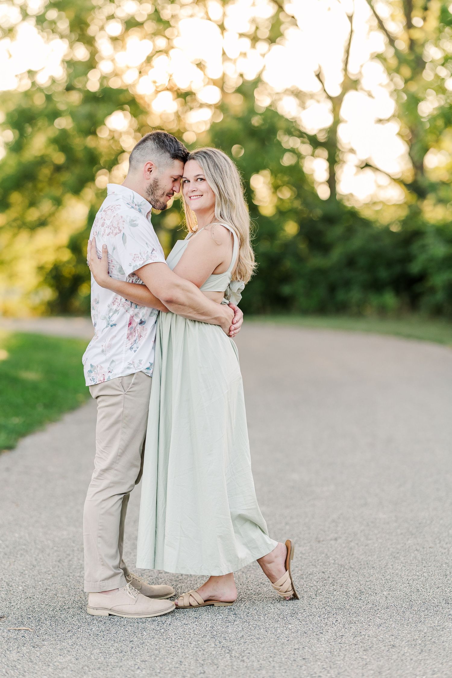 A romantic couple embraces on a peaceful park path during golden hour.