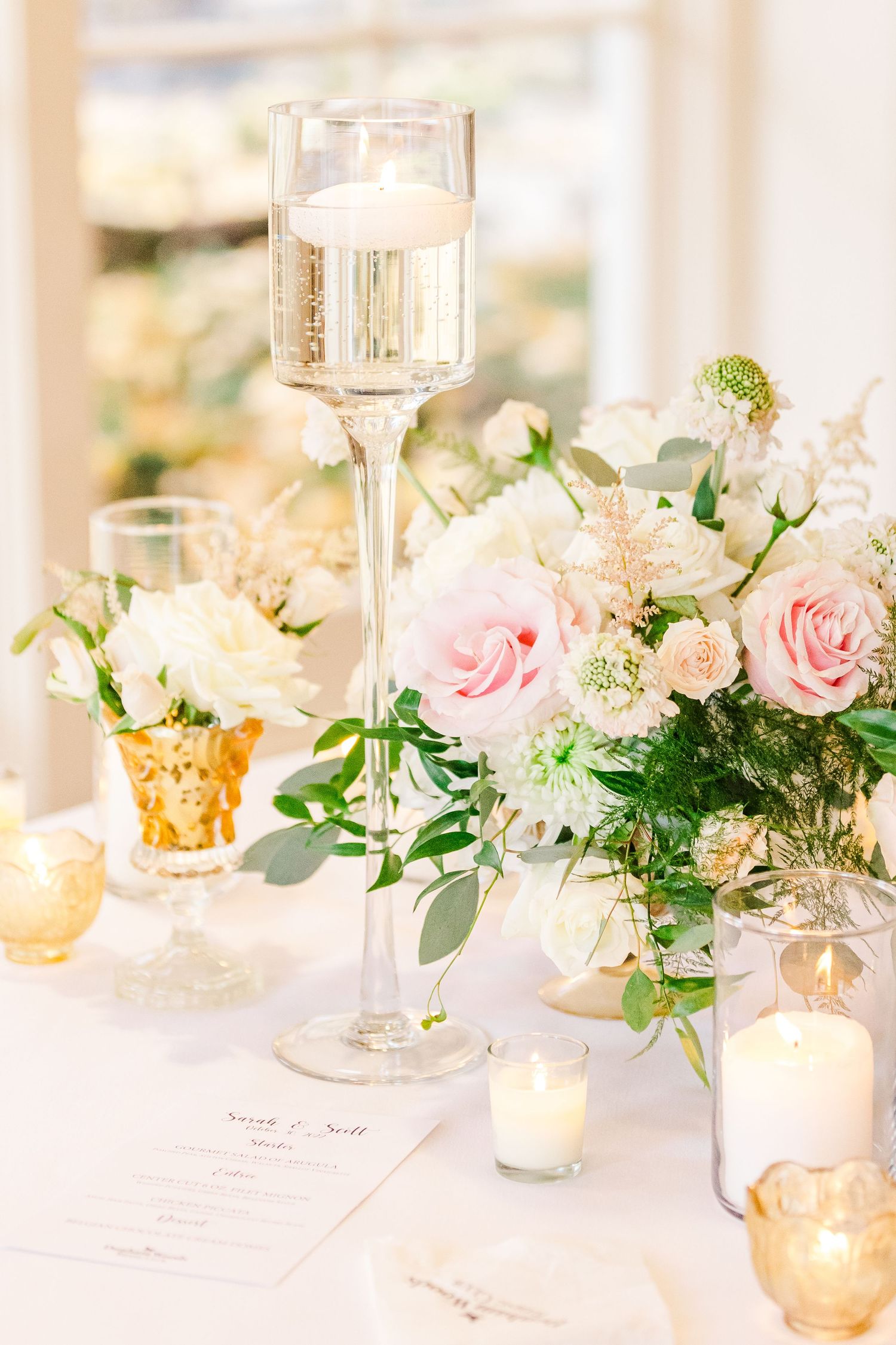 Elegant table setting with pink roses, candles, and champagne glasses for wedding reception.