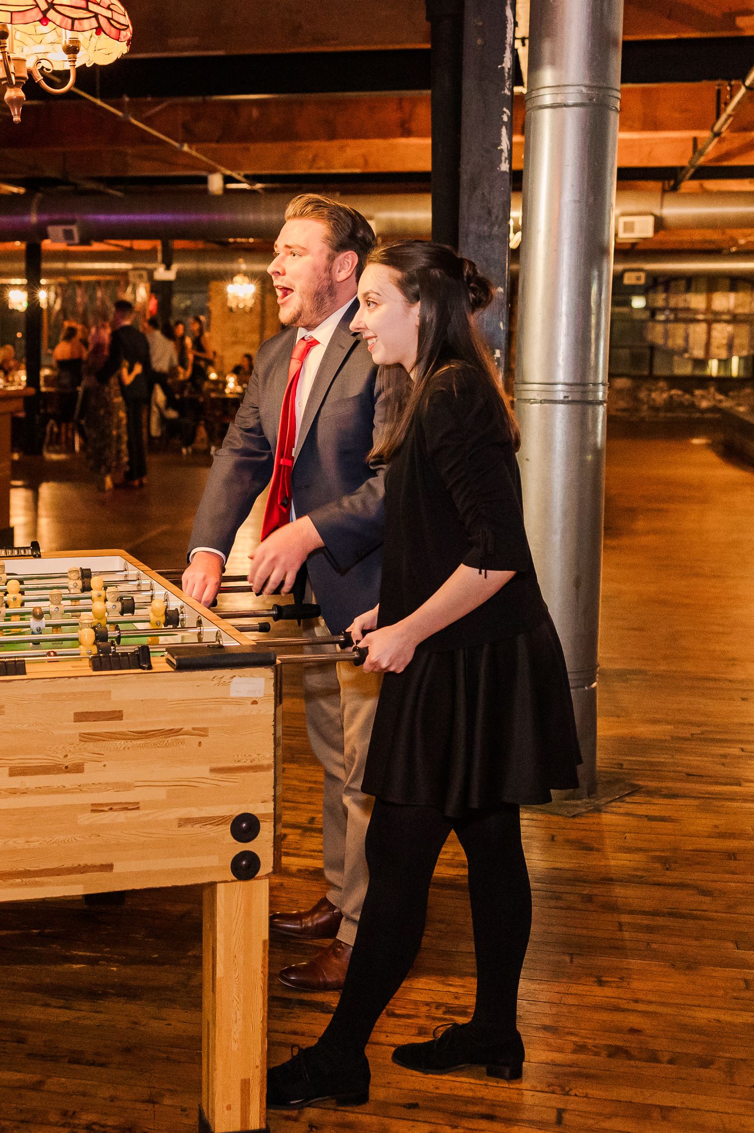 Wedding guests enjoying a game of foosball at a rustic venue with exposed brick walls.