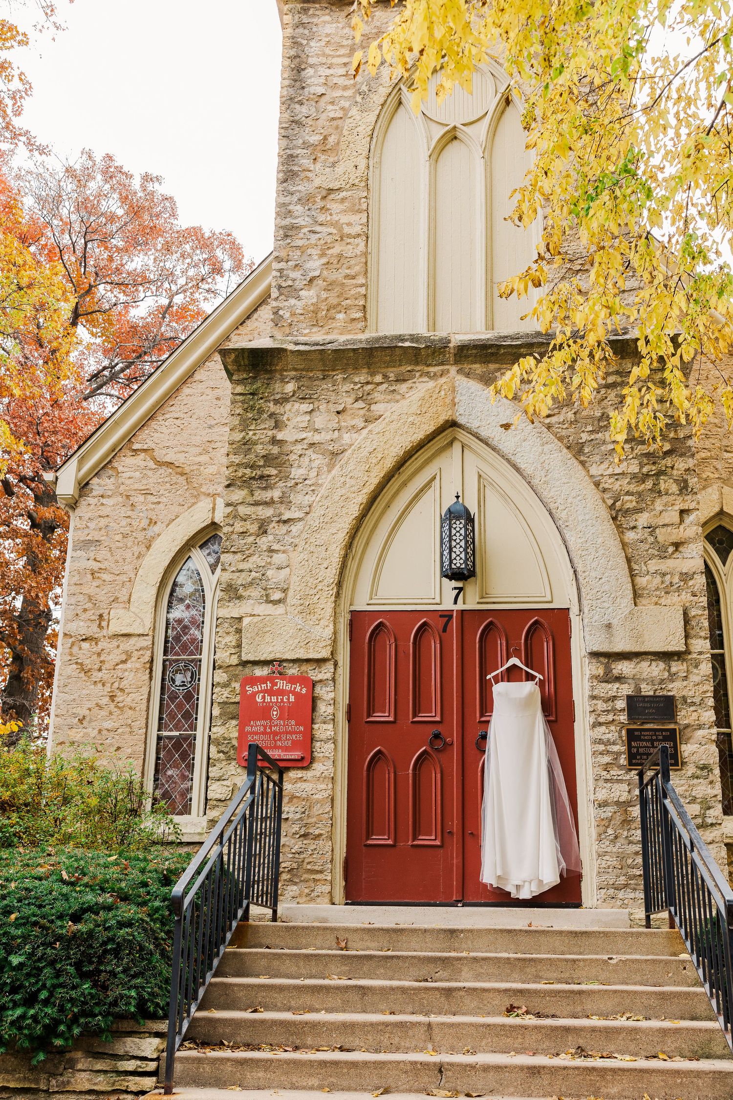 Stone church exterior with red door, fall foliage, and Gothic architectural details.