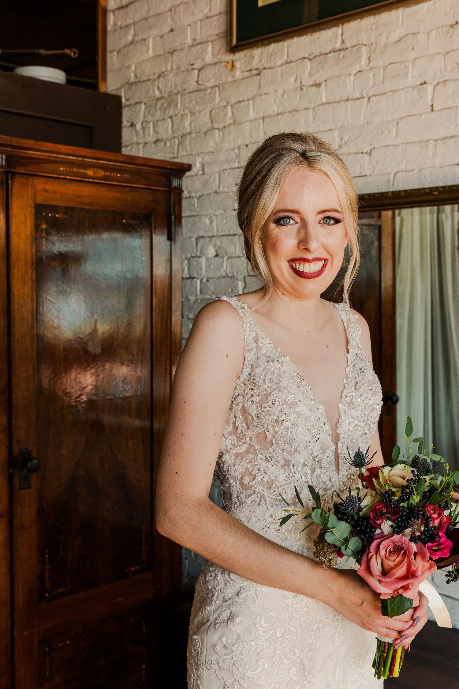 Elegant bridal portrait with colorful bouquet against white brick wall.