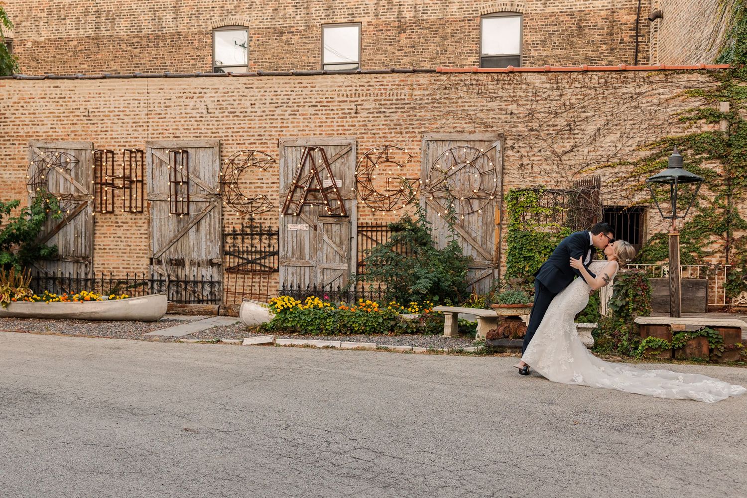 A couple shares a romantic moment against a brick wall with decorative iron gates and garden elements.