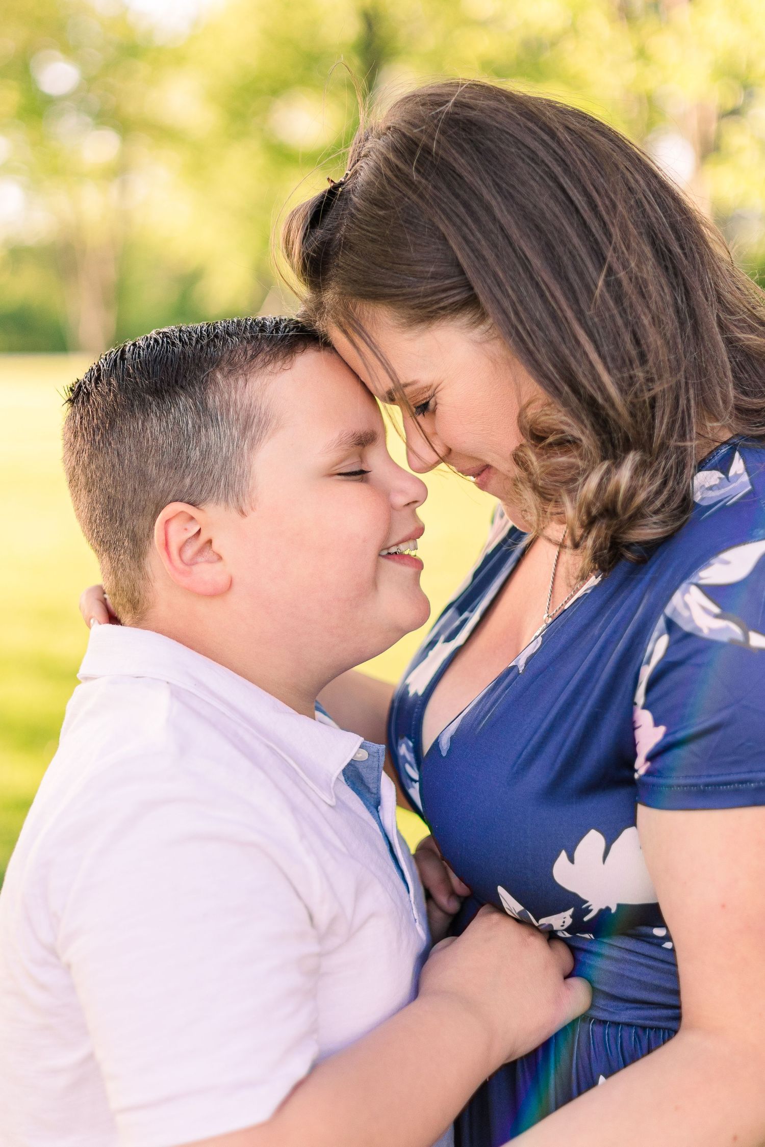 Touching foreheads in tender moment against blurred nature background with blue floral dress detail.