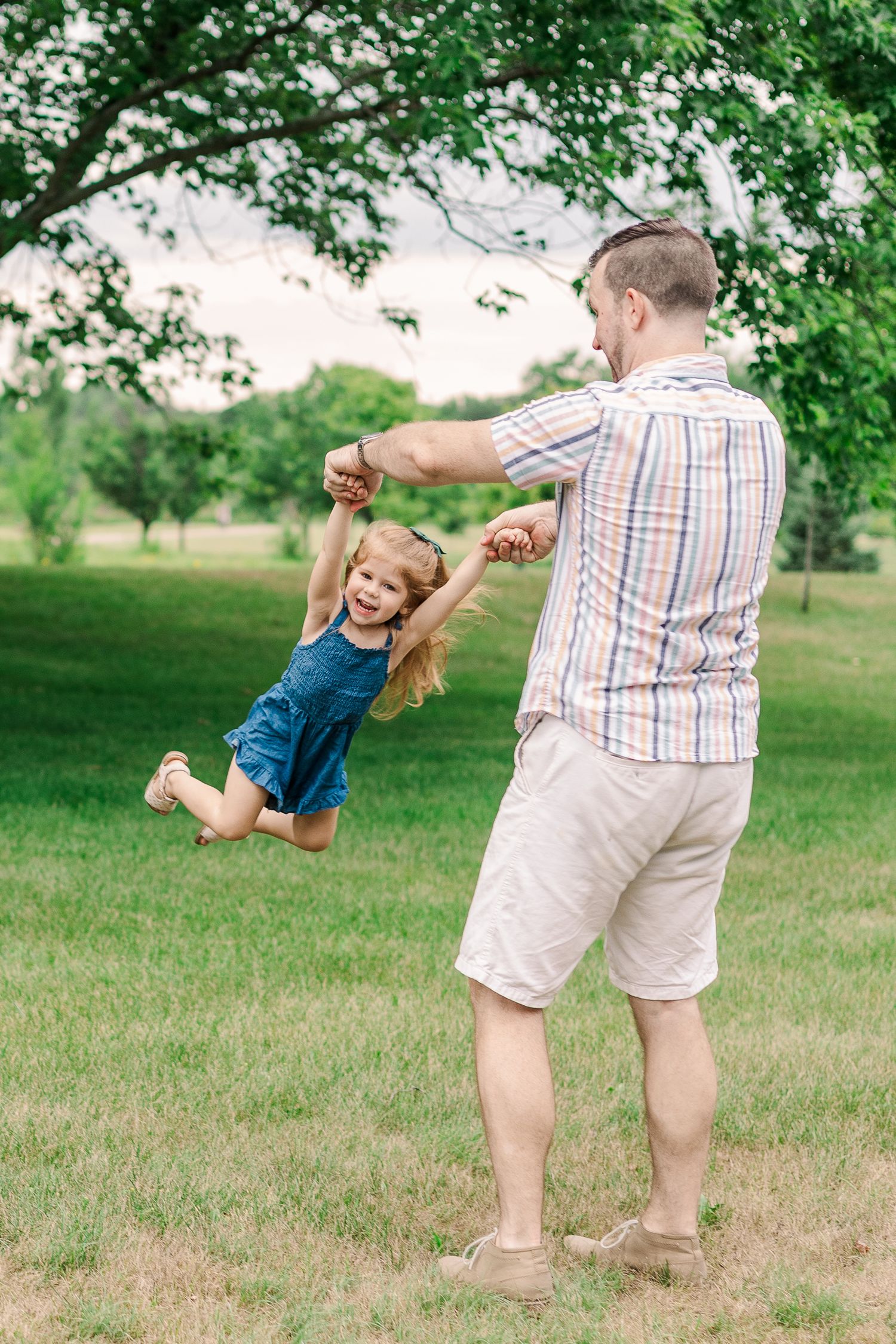 A playful moment captured as a child is swung around by an adult in a sunny park setting.