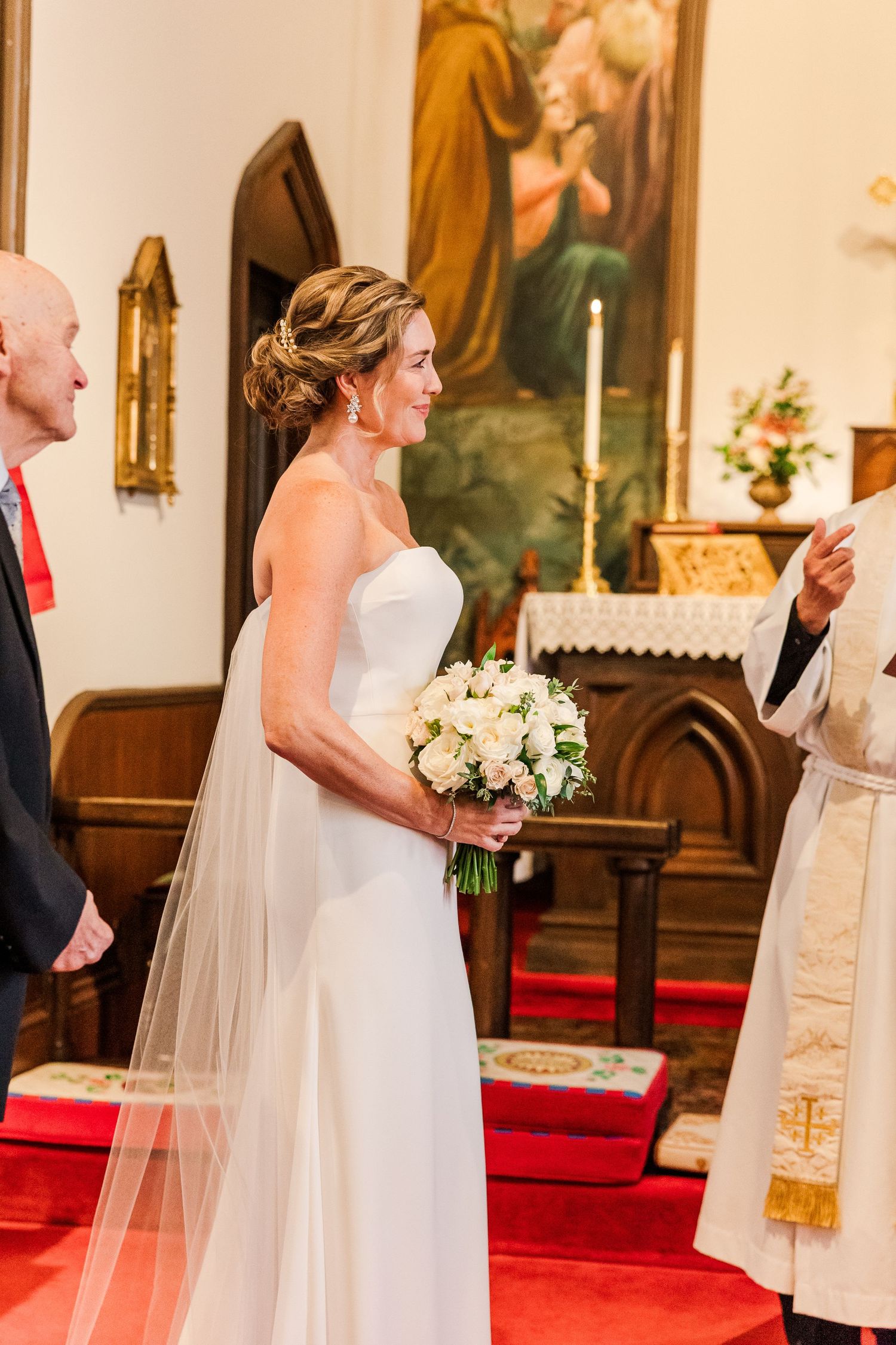A traditional church wedding scene with bride in white gown holding bouquet near religious artwork.