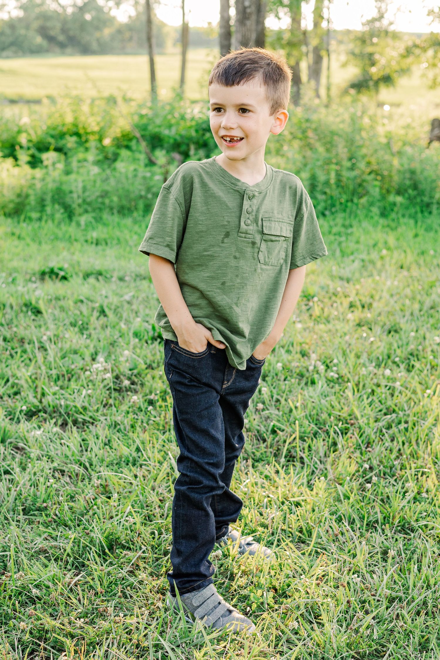 Young person standing in a grassy field wearing a green t-shirt and jeans.