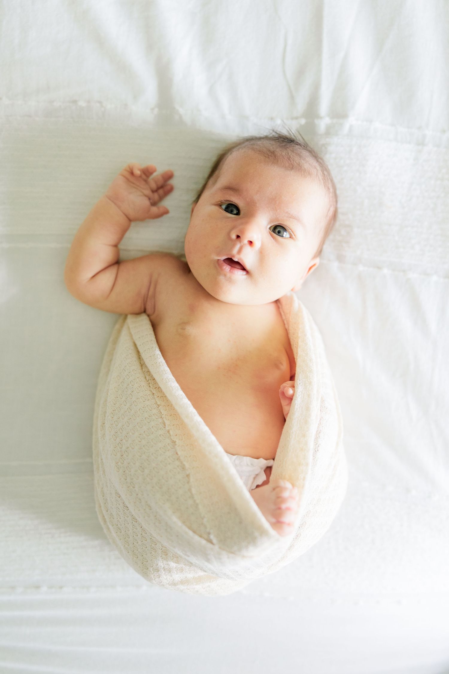 Newborn baby girl wrapped in a white swaddle on the bed during a lifestyle newborn session at home
