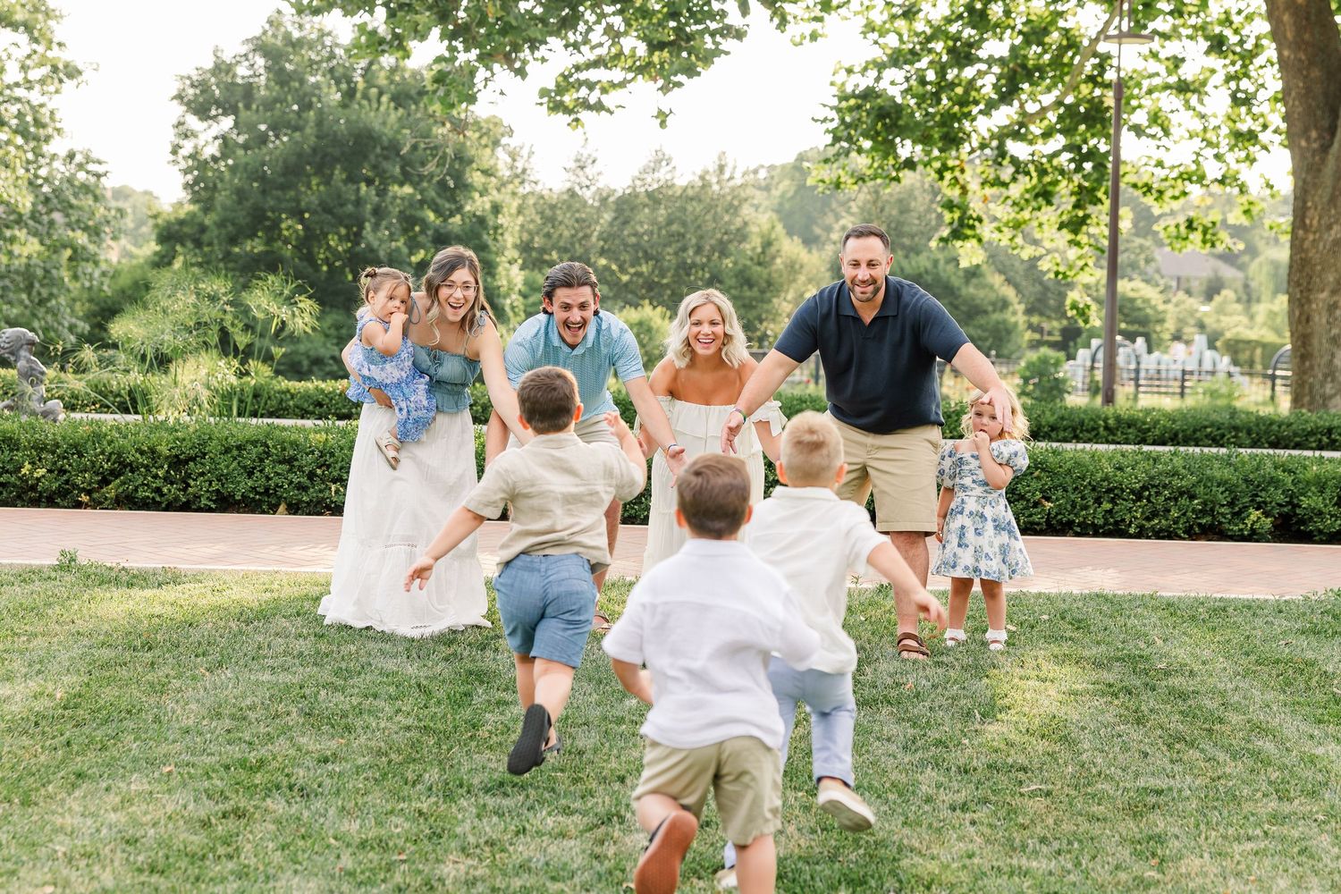 Family with young children playing outdoors in a lush green park, laughing and running together on a sunny day.
