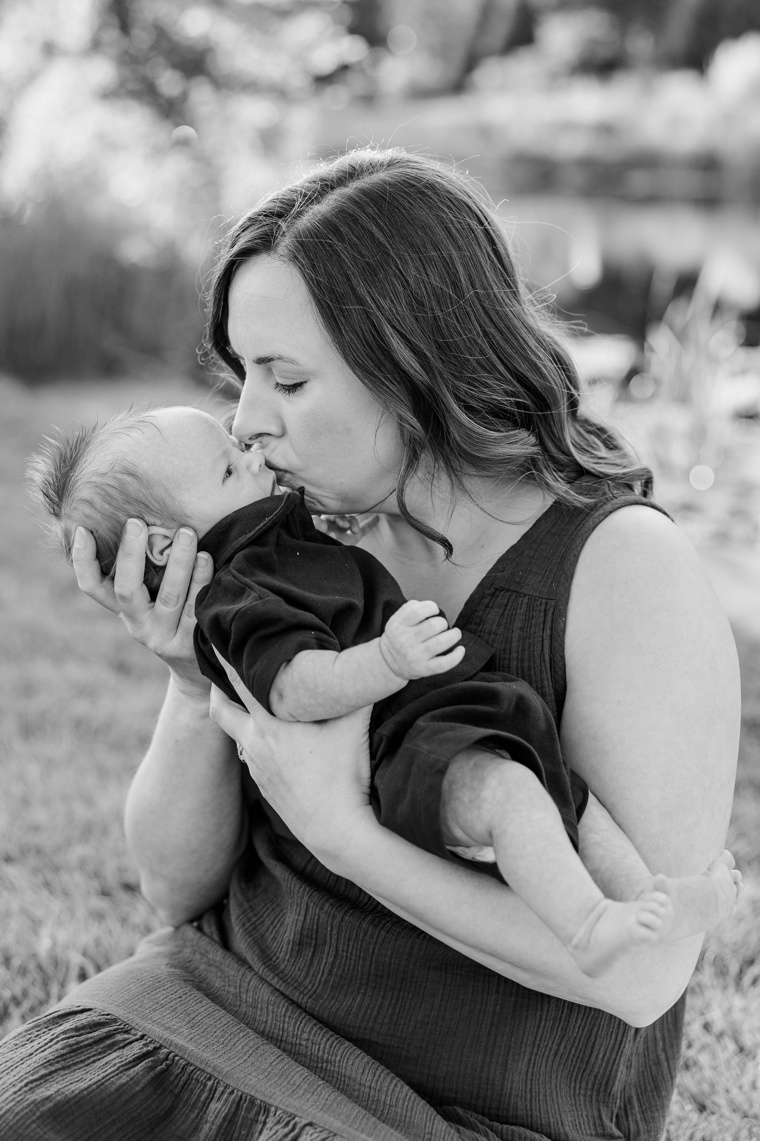 Black-and-white portrait of Hilary kissing newborn Lincoln while cradling him in her arms.