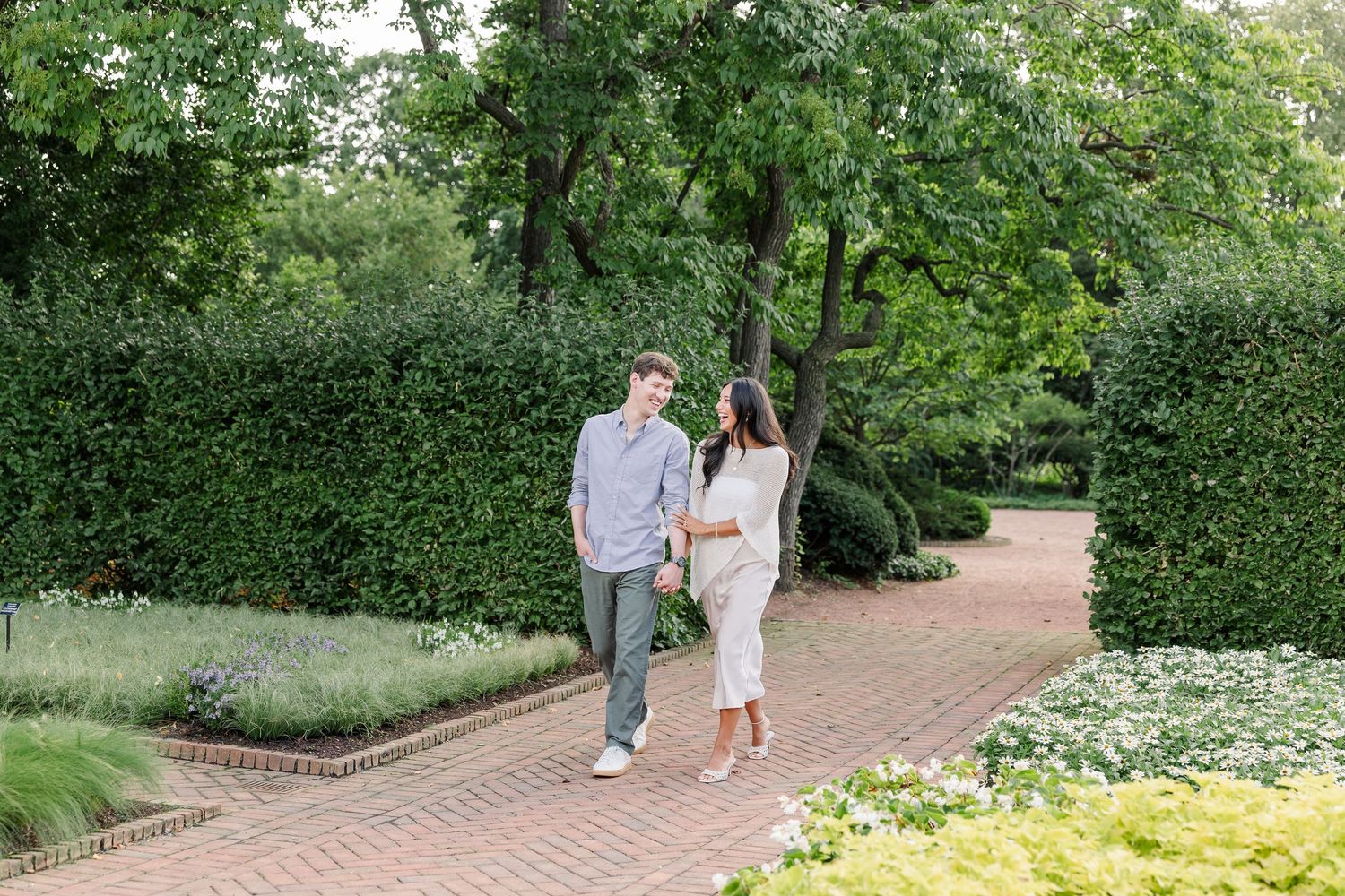 Alysia and Jack stroll together along a flower-lined pathway after their proposal.