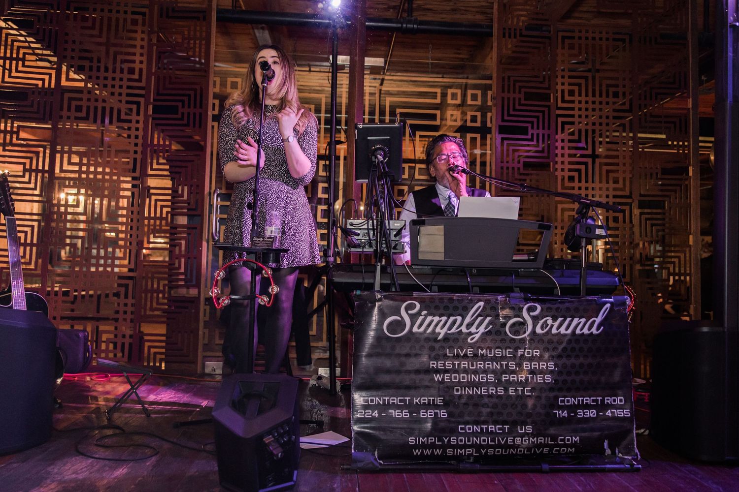 Live band performing at event with geometric pattern backdrop and purple lighting.