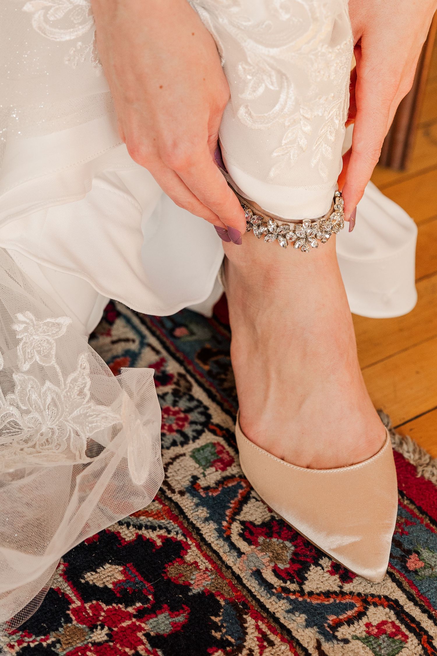 Detailed shot of an ornate ankle bracelet being fastened over nude heels on a patterned rug.
