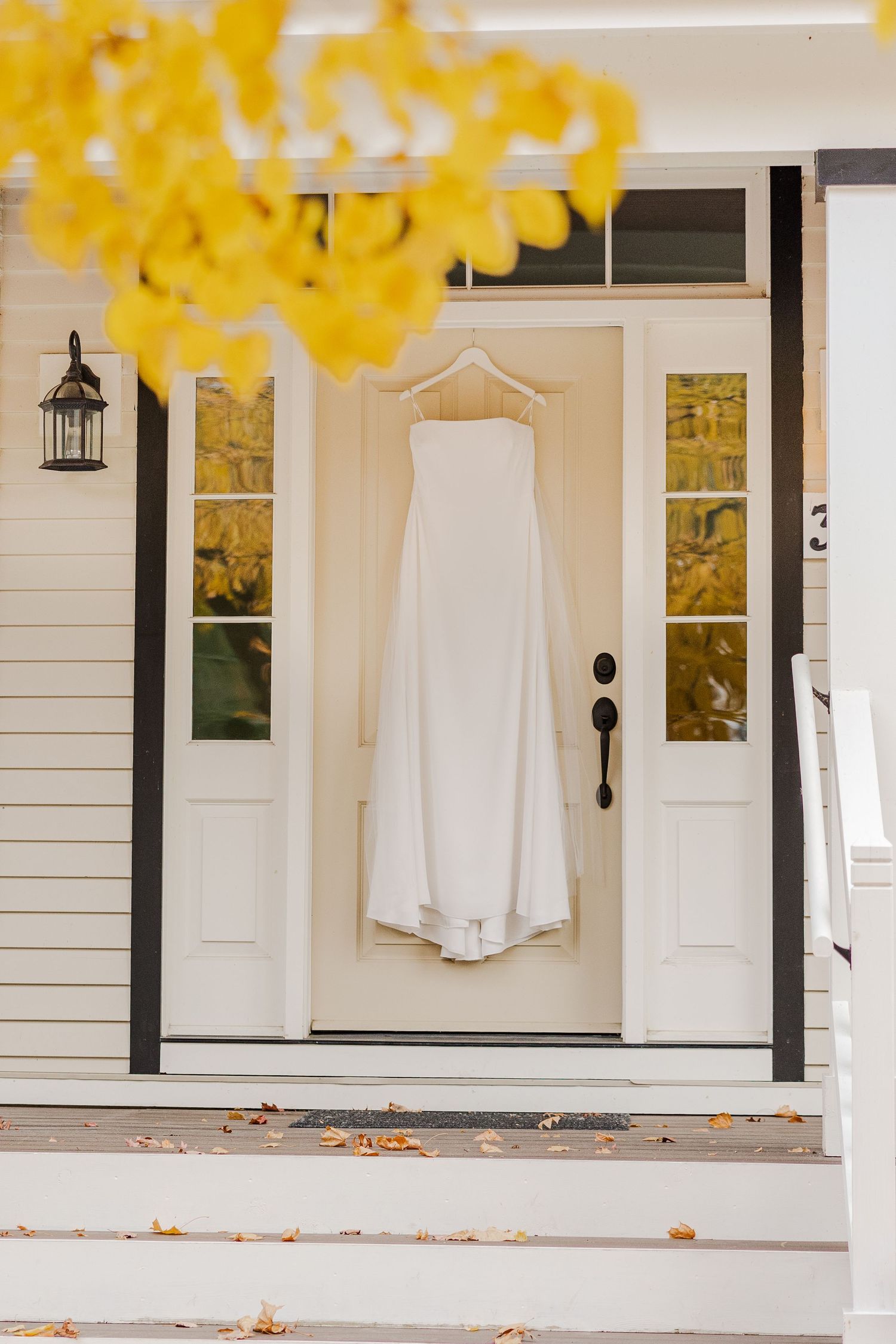 Wedding dress hanging on front door with yellow fall foliage in background.