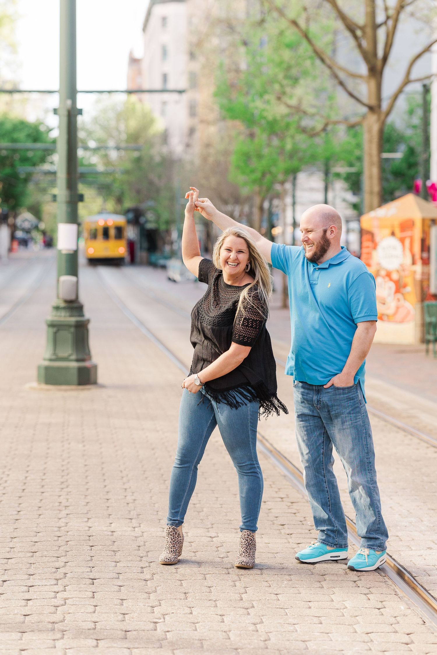 A couple dances playfully on cobblestone streets with trolley tracks.