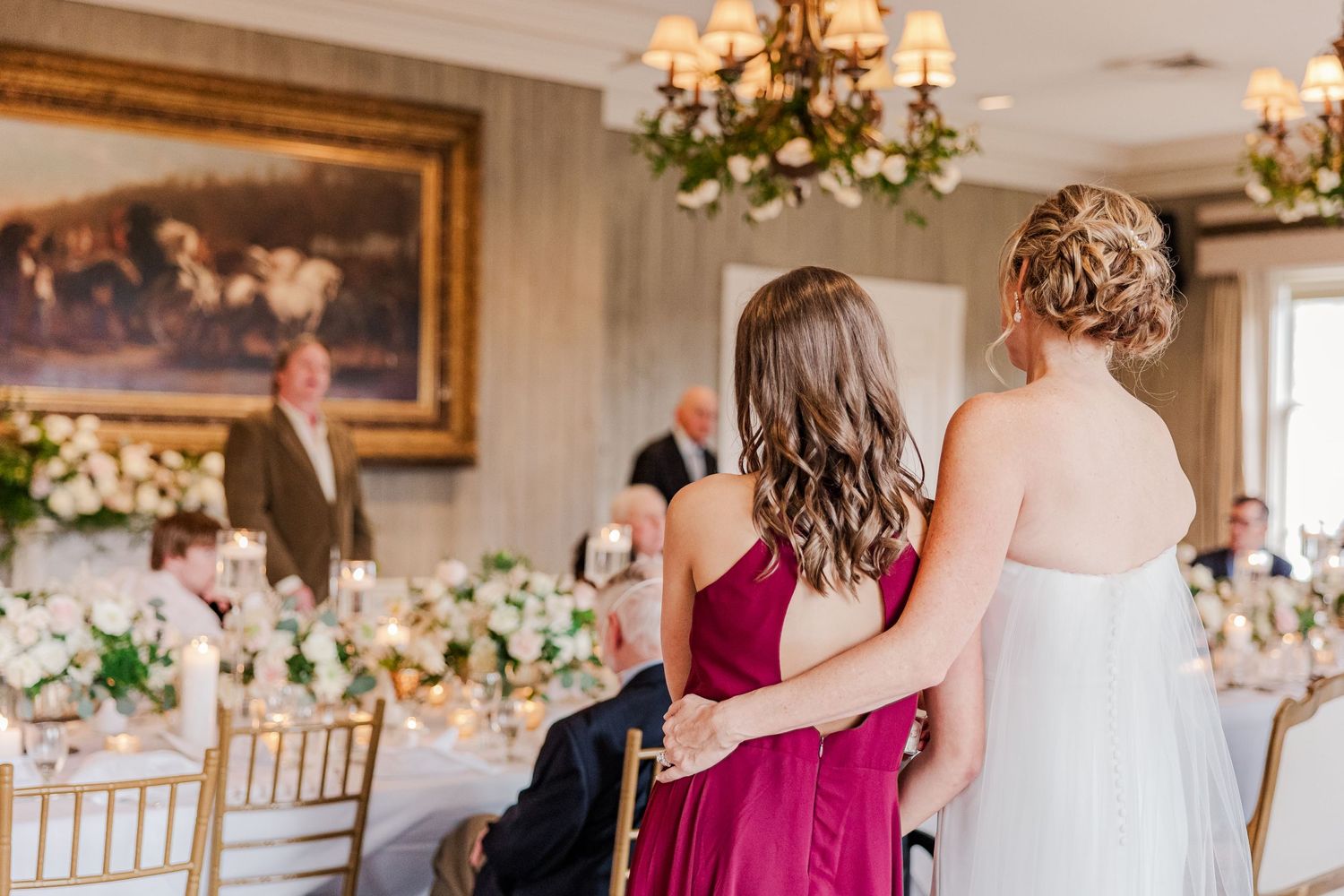 Wedding reception venue with elegant chandeliers and floral centerpieces on white tablecloths.