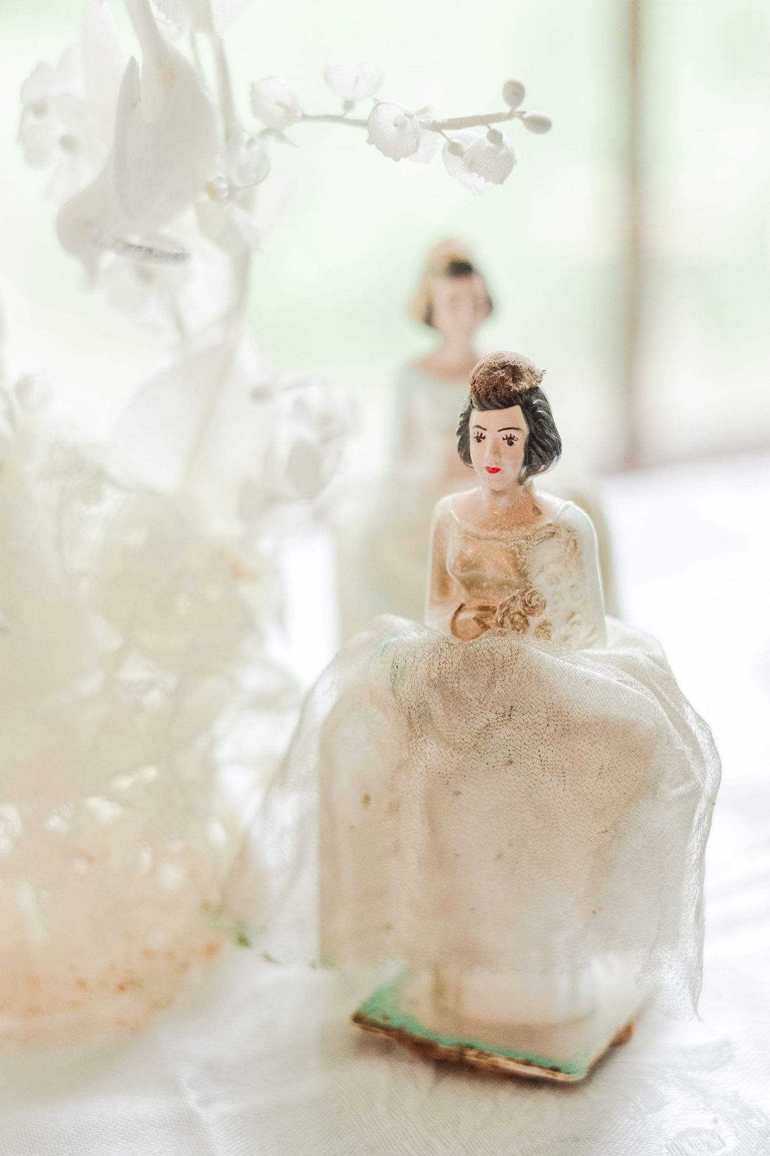 Vintage-style wedding cake topper figurine in white dress with floral backdrop.