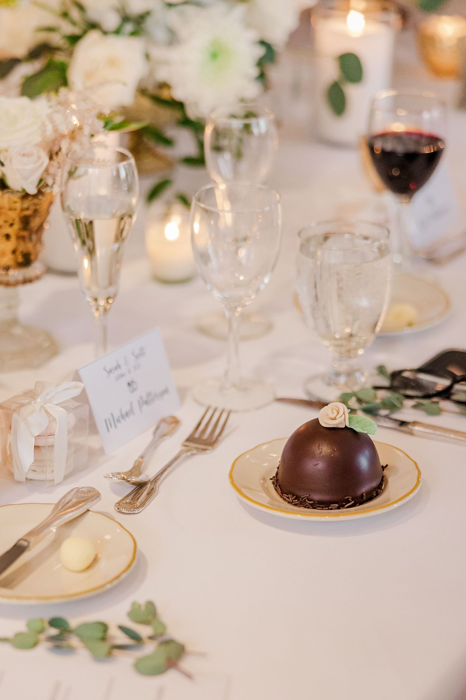 Elegant place setting with chocolate dome dessert, wine glasses, and floral decorations.
