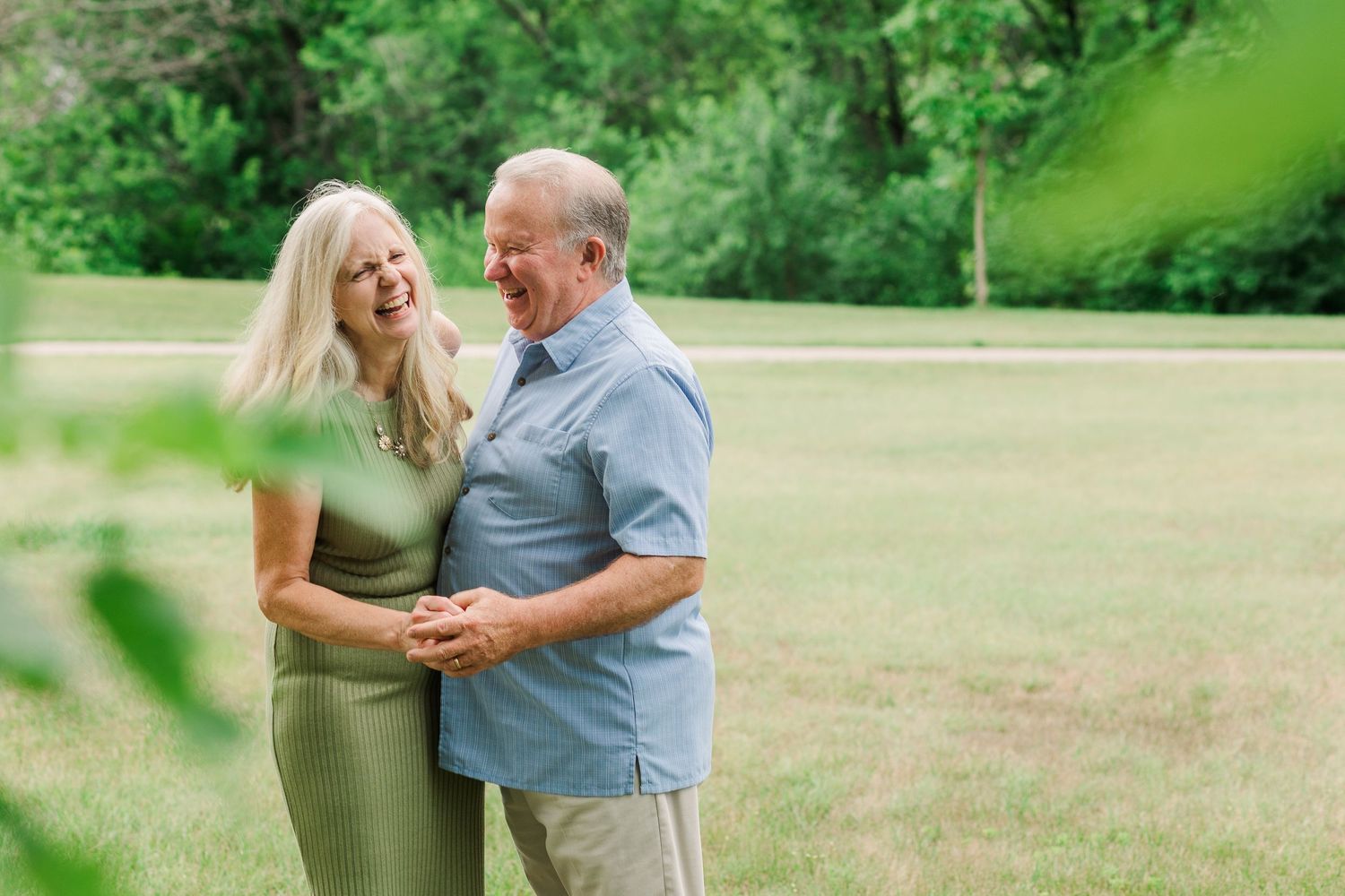 A loving couple embraces while standing in a sunny green field.