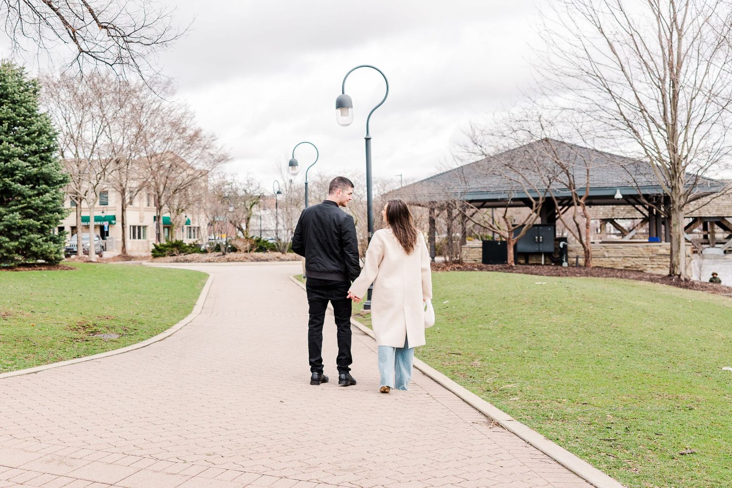 A couple walking along a curved path in a park with lamp posts on an overcast day.