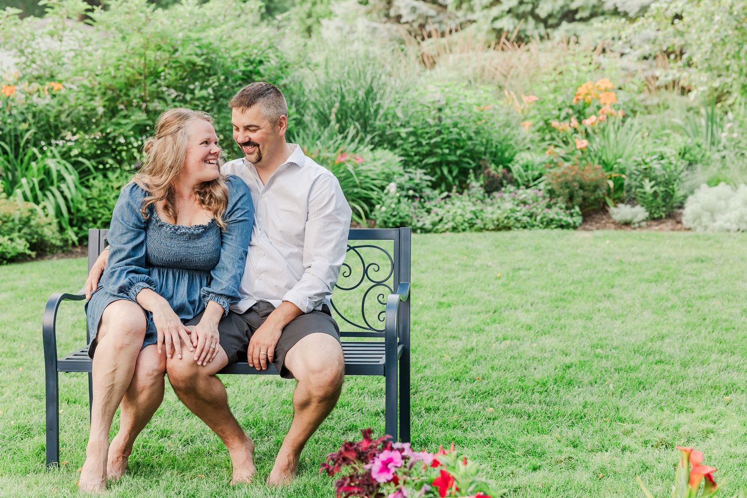 Couple sharing a candid laugh while sitting on an ornate bench in a blooming garden.
