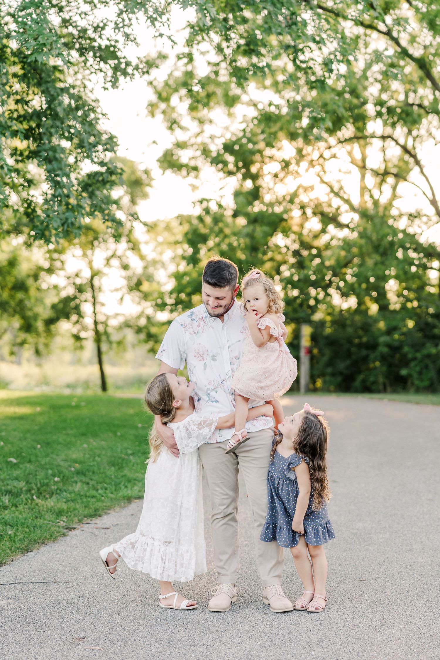Sweet family portrait taken on tree-lined path during summer evening.